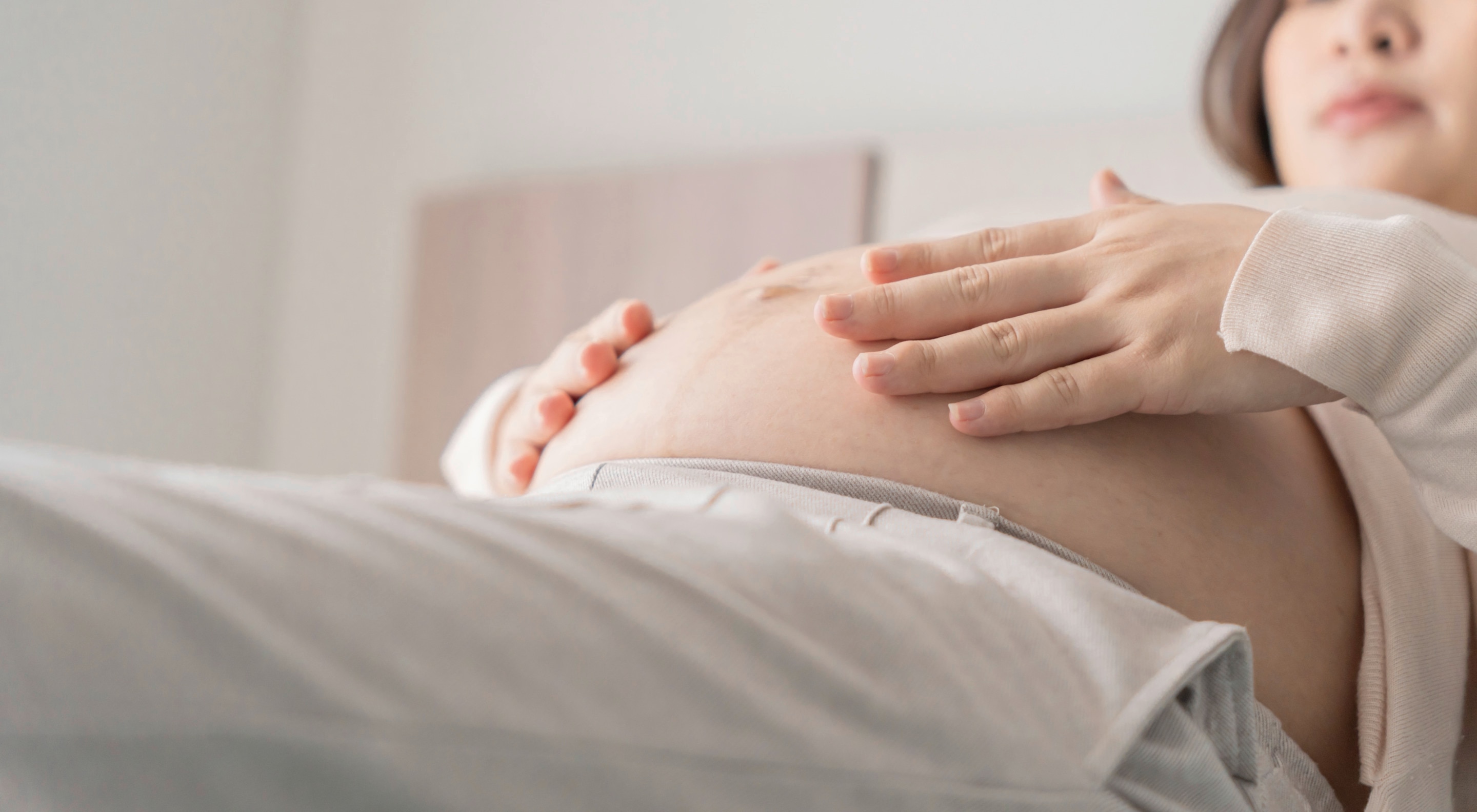 A pregnant Asian woman holding her belly while lying down.