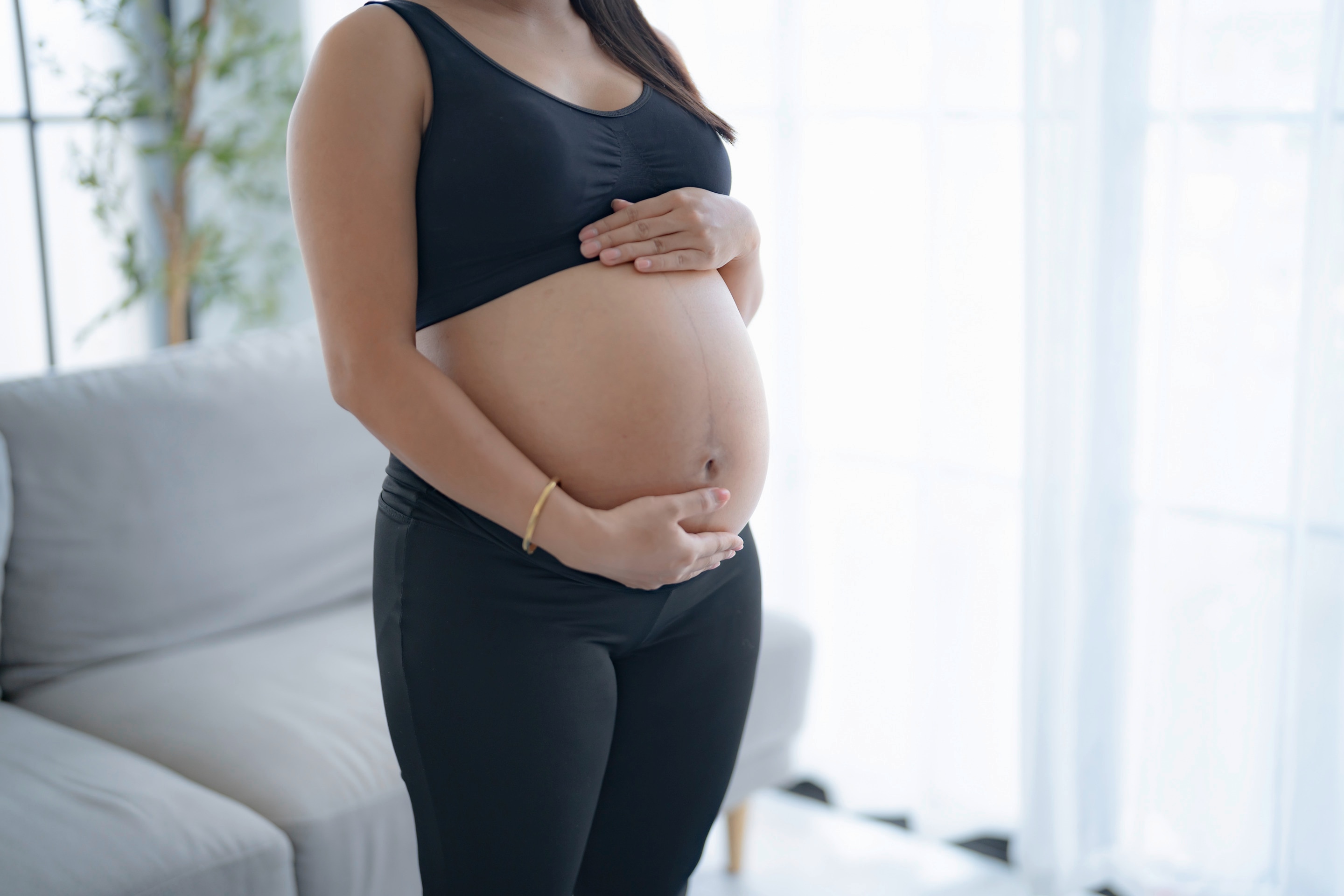 A pregnant Asian woman holding her belly while standing.