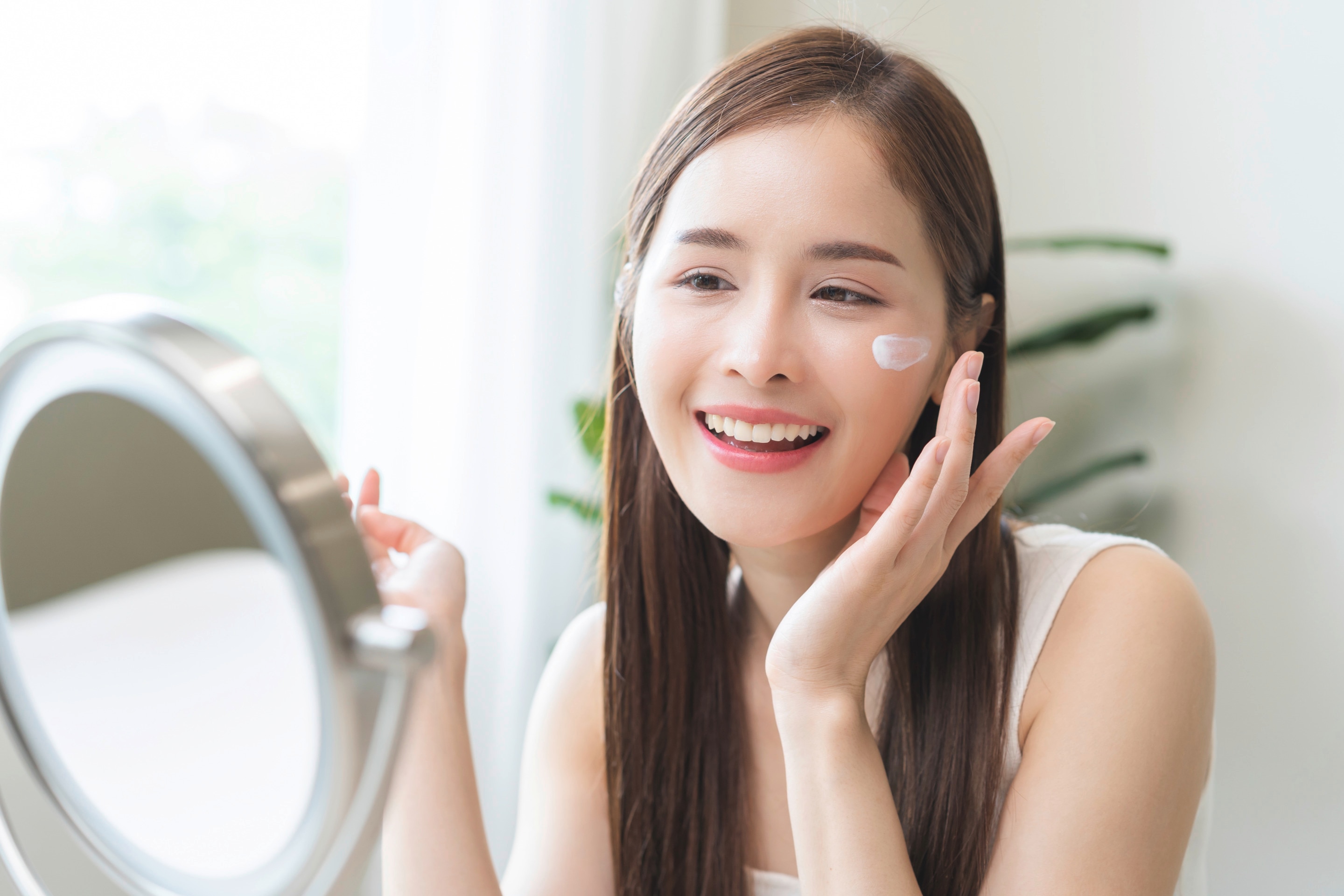 Smiling woman applying cream to her cheek happily. 