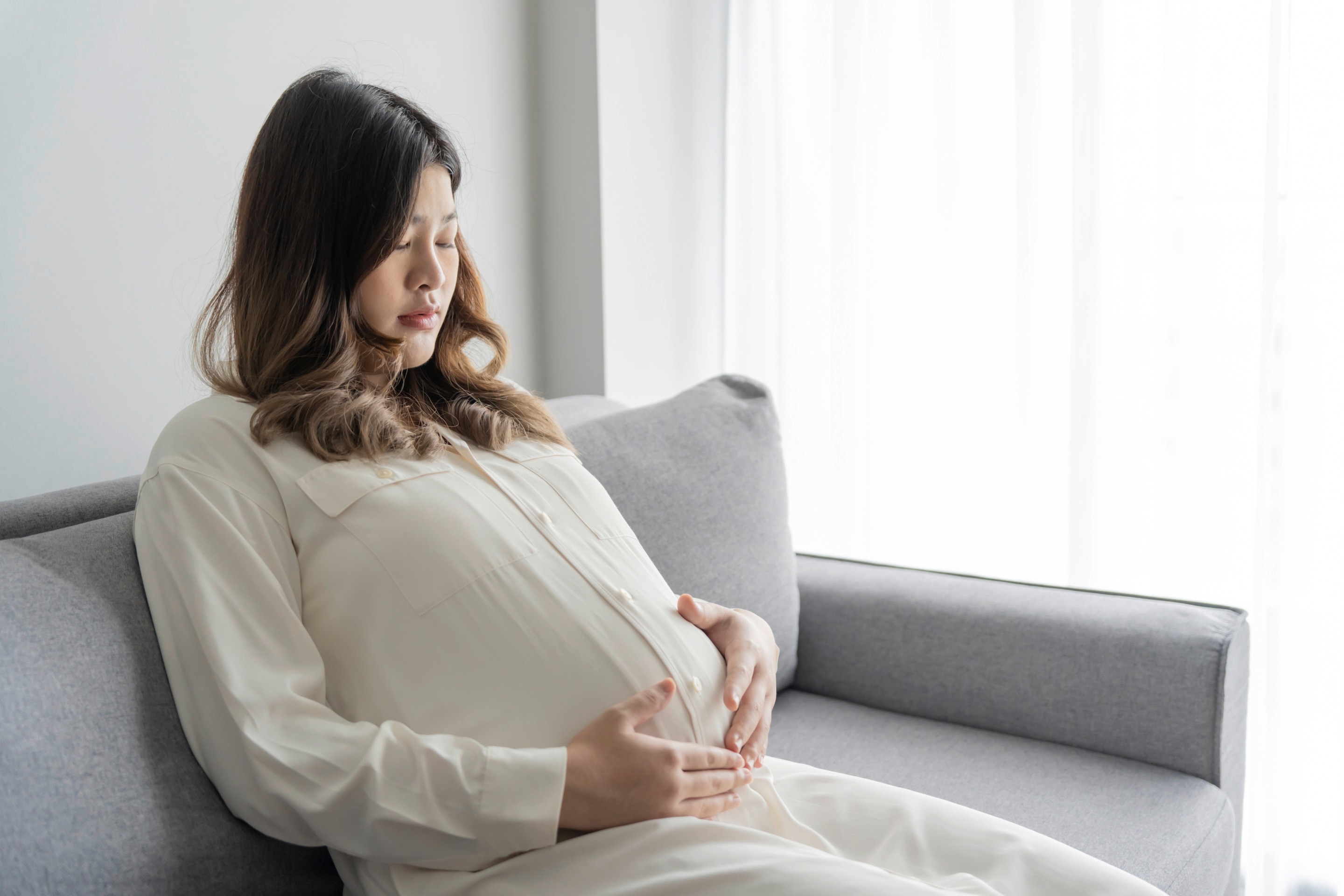 Pregnant woman looking down at her belly while sitting on a sofa.