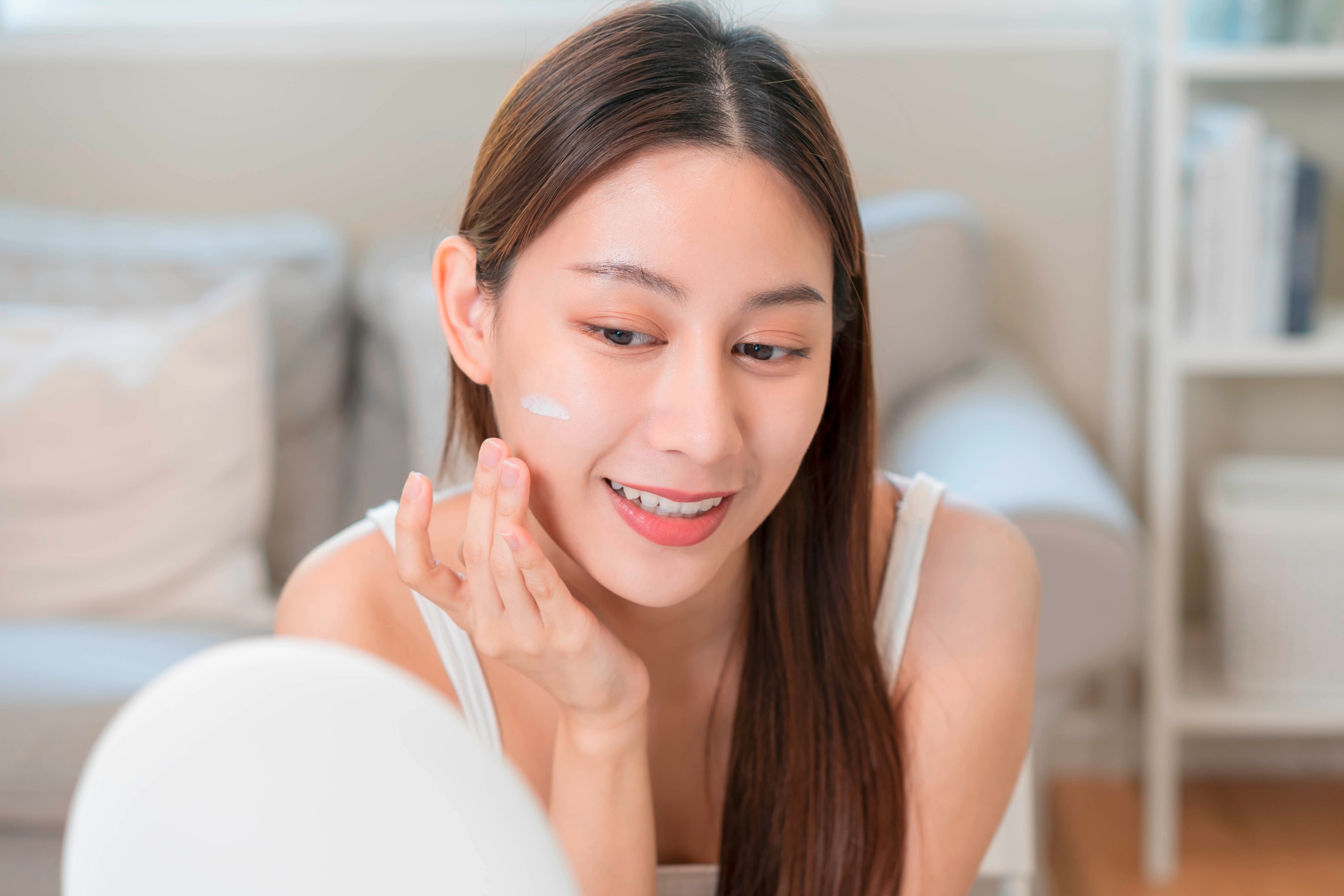 An Asian woman doing skincare in front of a table stand mirror.
