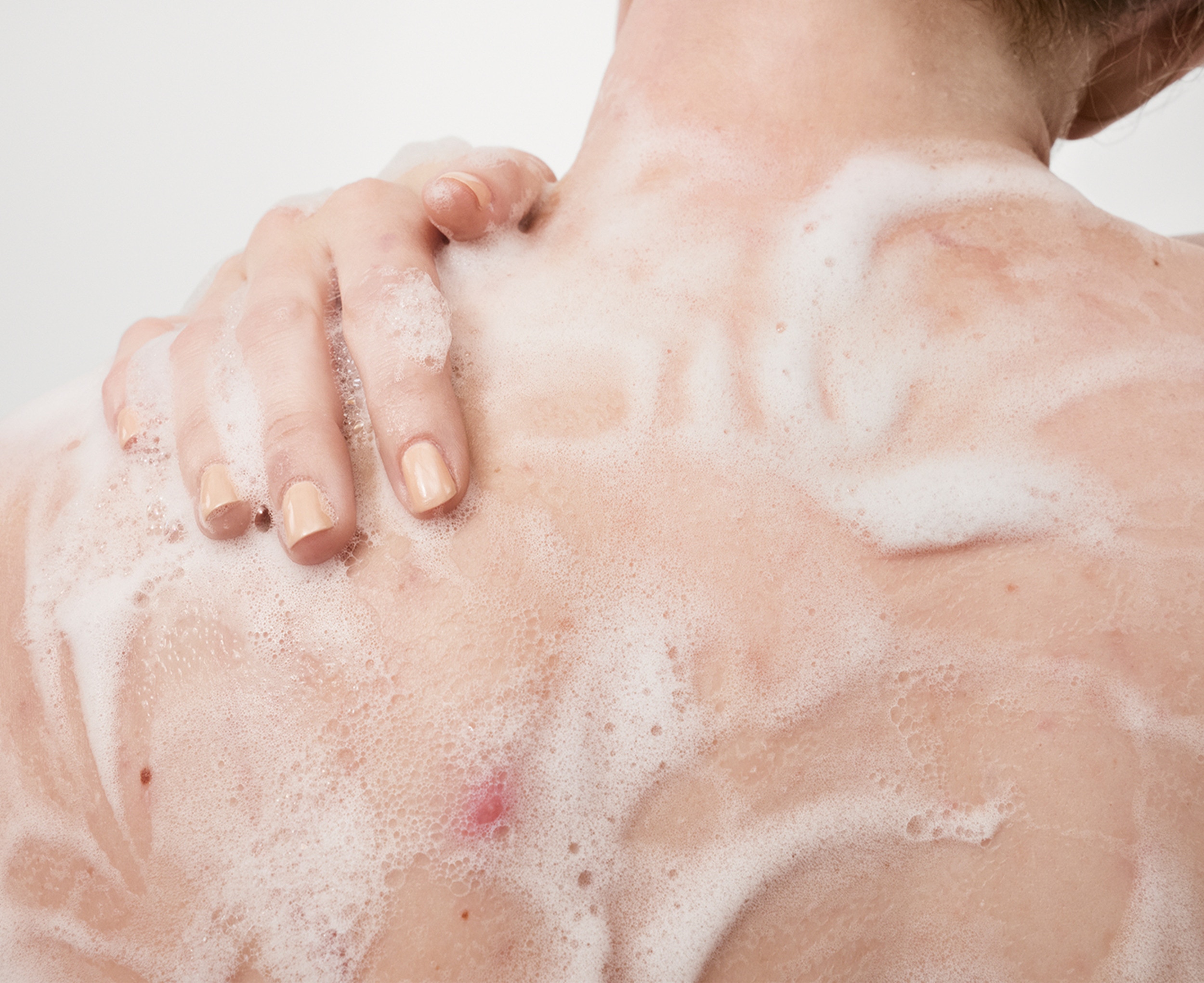 Image of the back of a woman, using body wash which has been lathered 