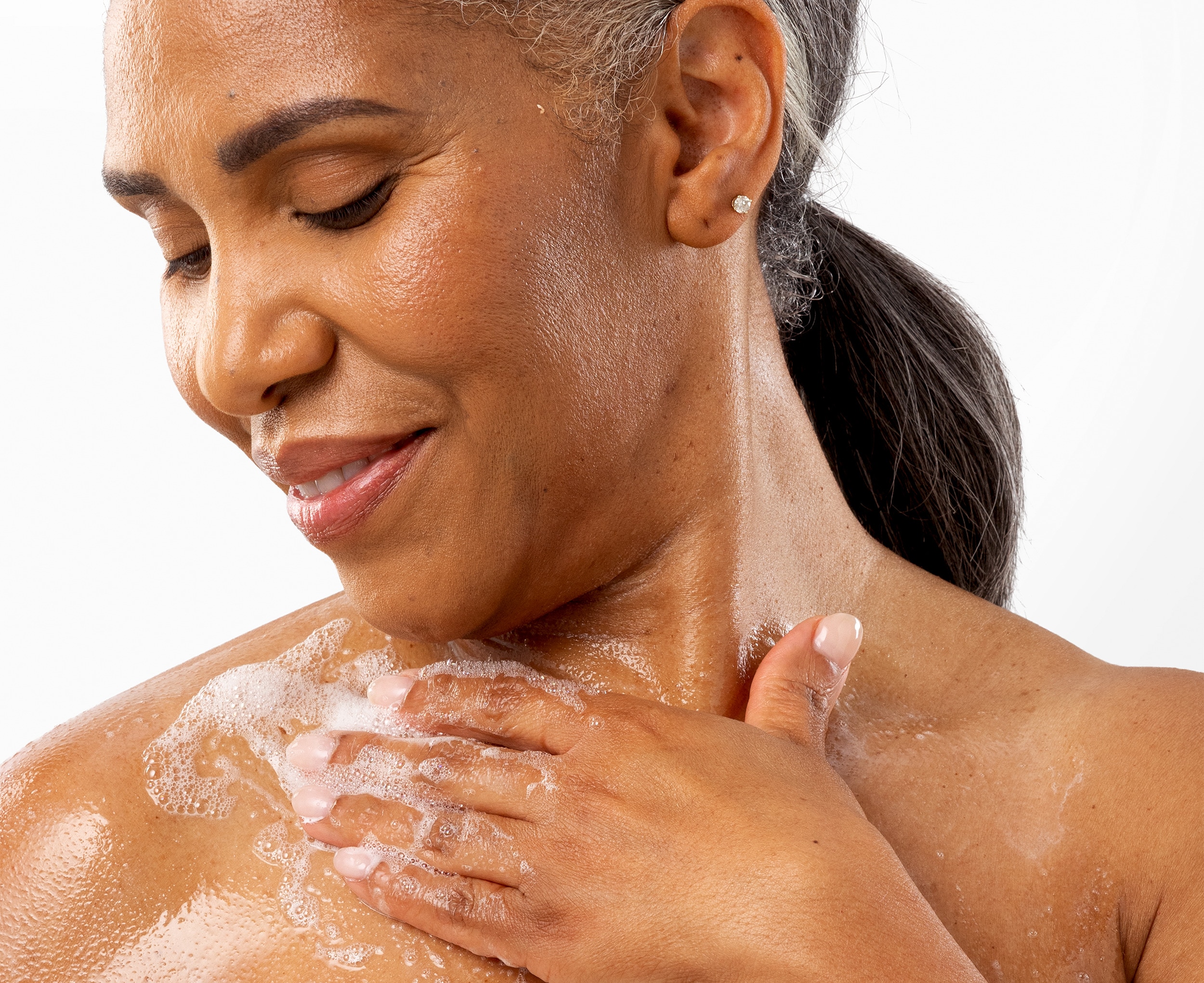 A woman lathering body wash on her upper shoulder
