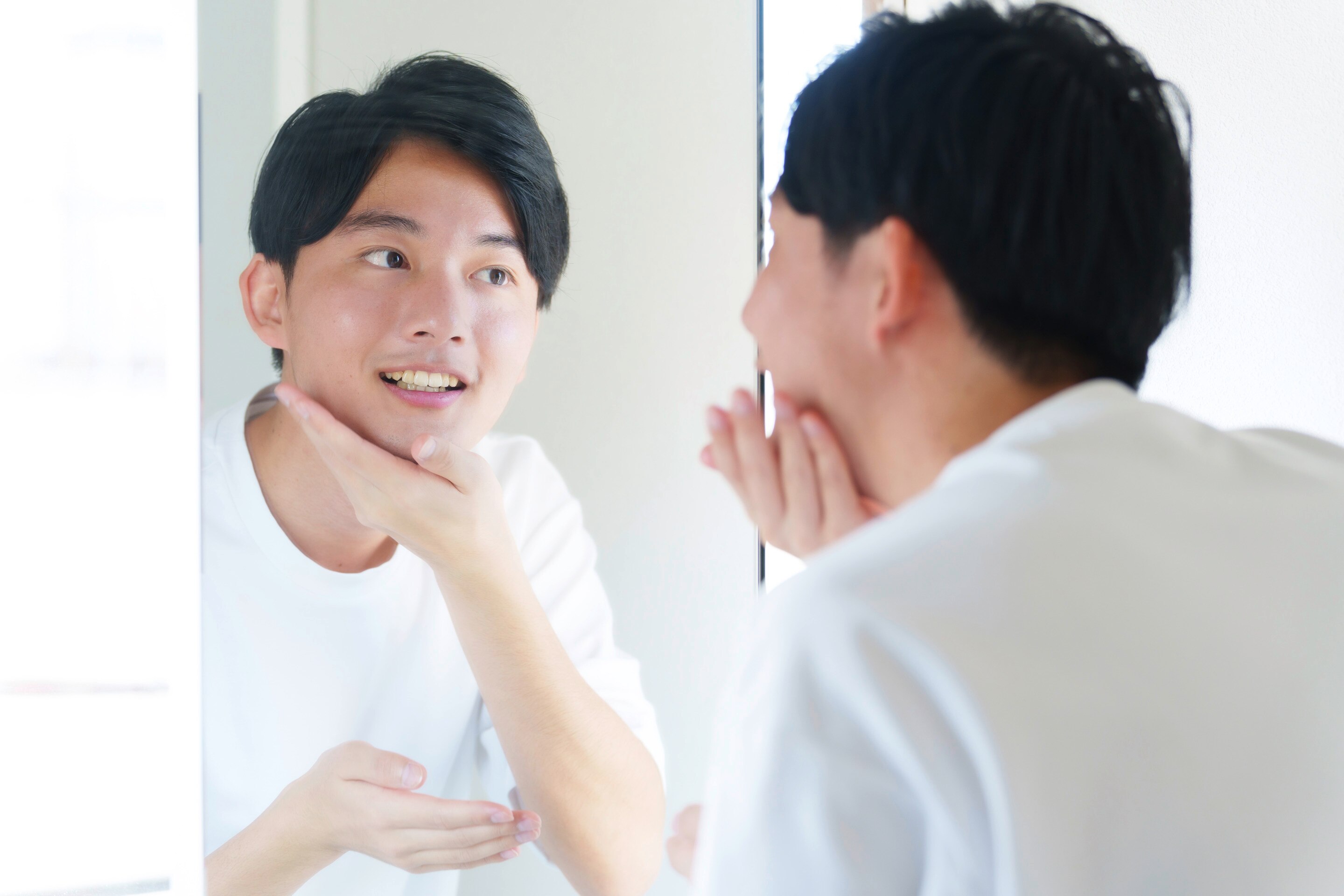 Closeup of an Asian man in white shirt looking at a mirror.