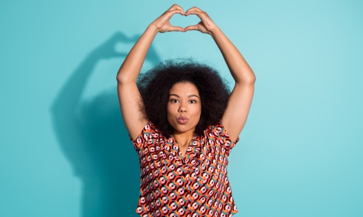 African American woman forming a heart above her head, showing her underarms because her deodorant is working.