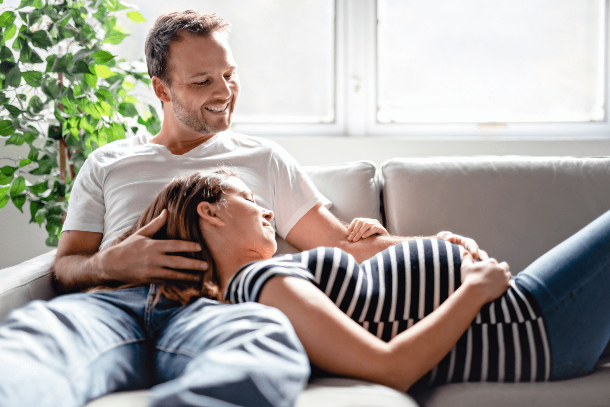 Happy couple relaxing on the couch while odor-free pregnant wife looks at her pregnant belly&nbsp;