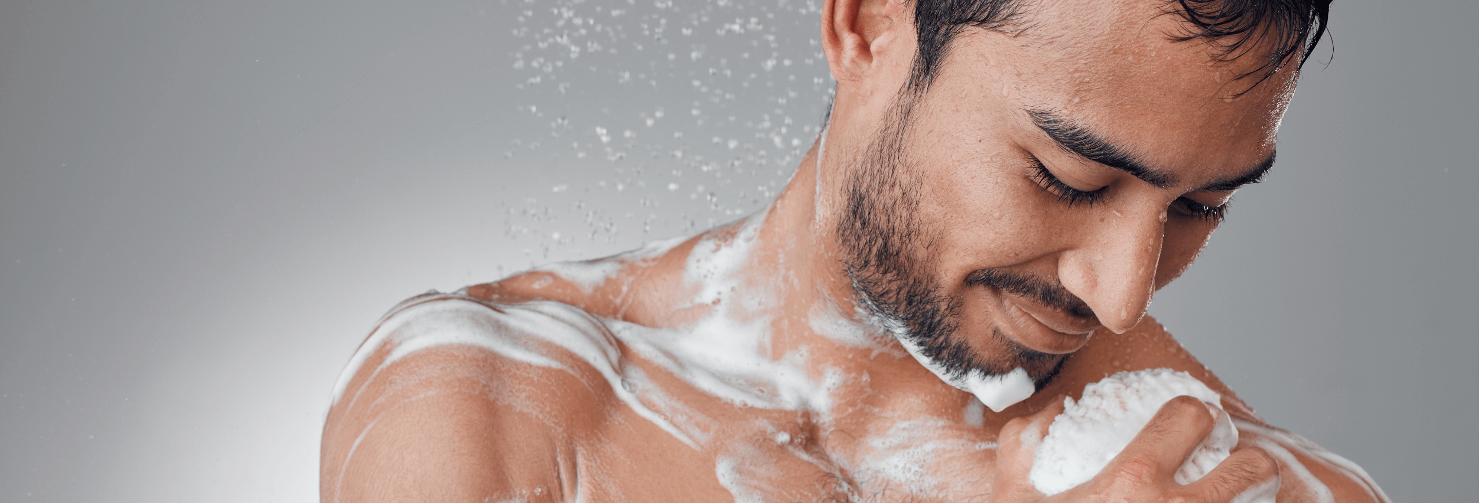 Young man lathering up in the shower with body wash that fights odor and sweat control