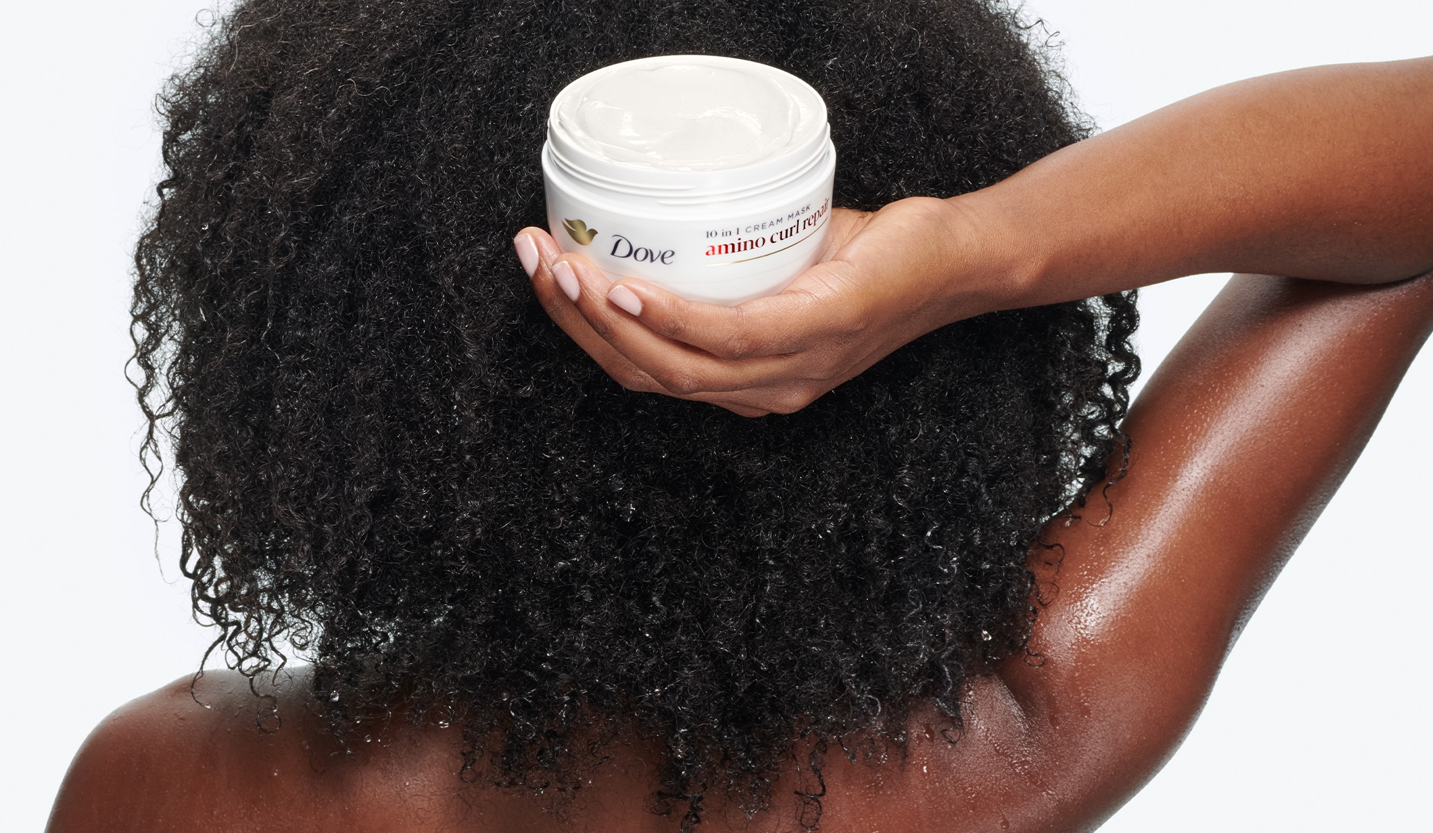 Woman with afro curly hair holding the Dove Amino Curl Hair Mask behind her head