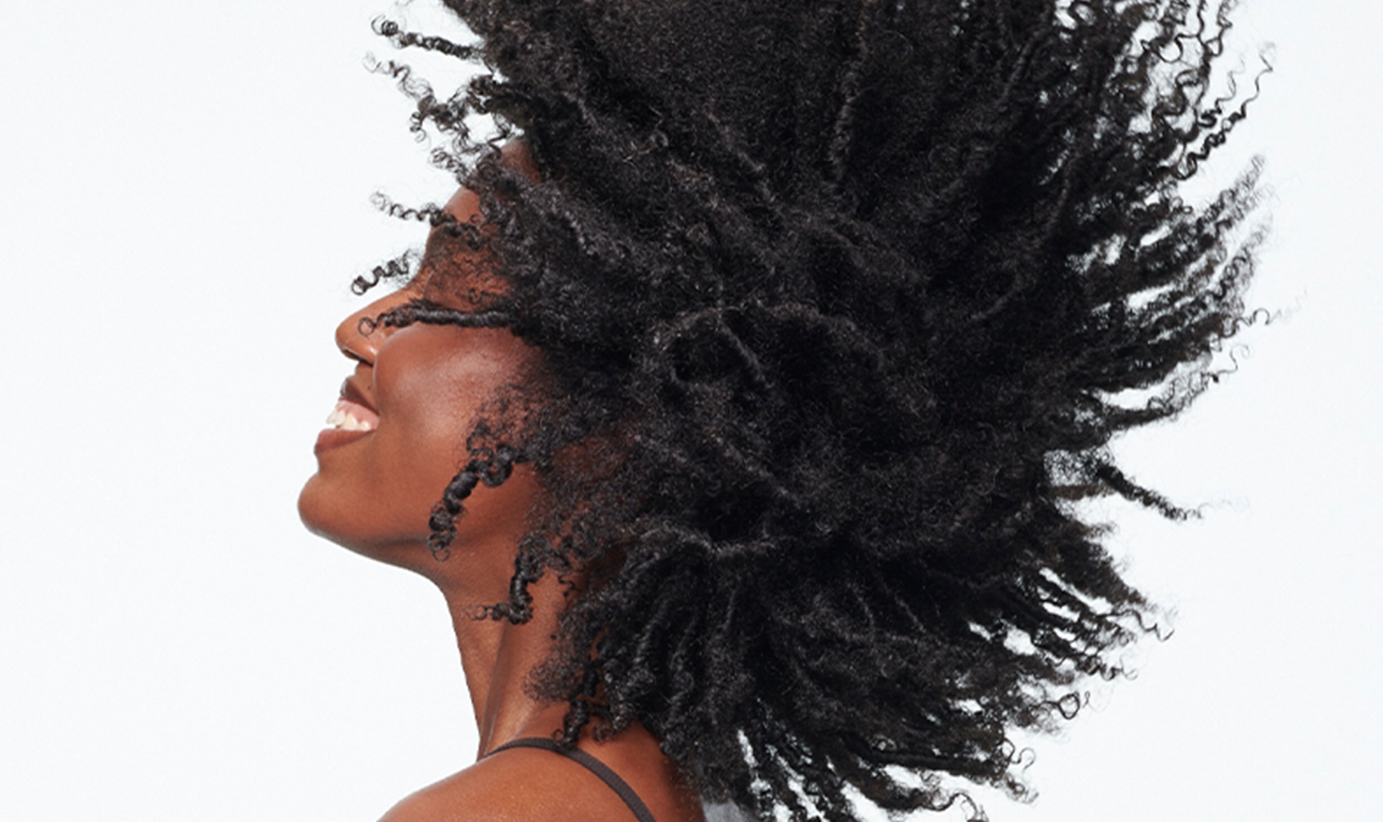 A woman with afro curly hair smiling whilst shaking her hair