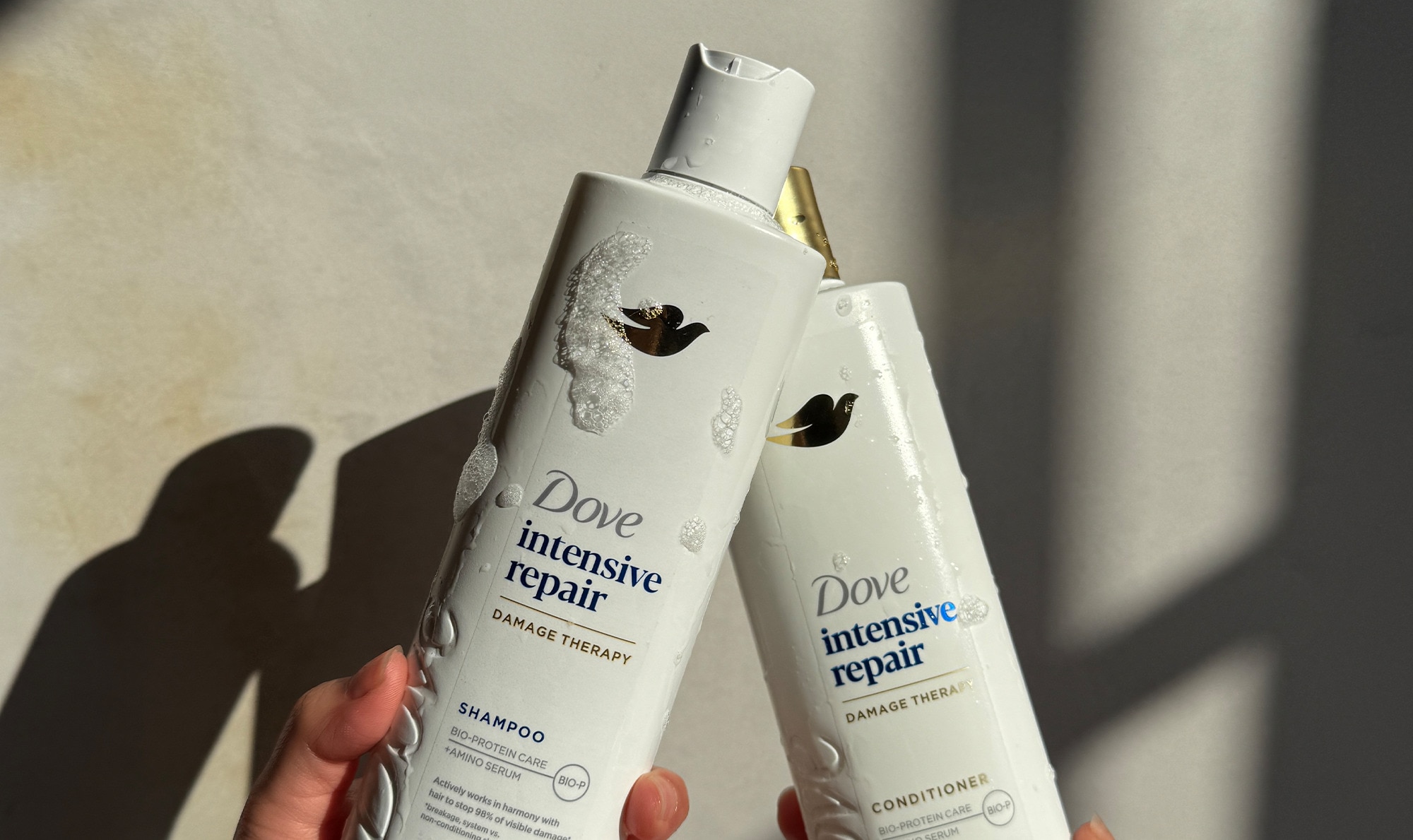 Hand holding the Intensive Repair Shampoo and Conditioner with studs of shampoo on the packs