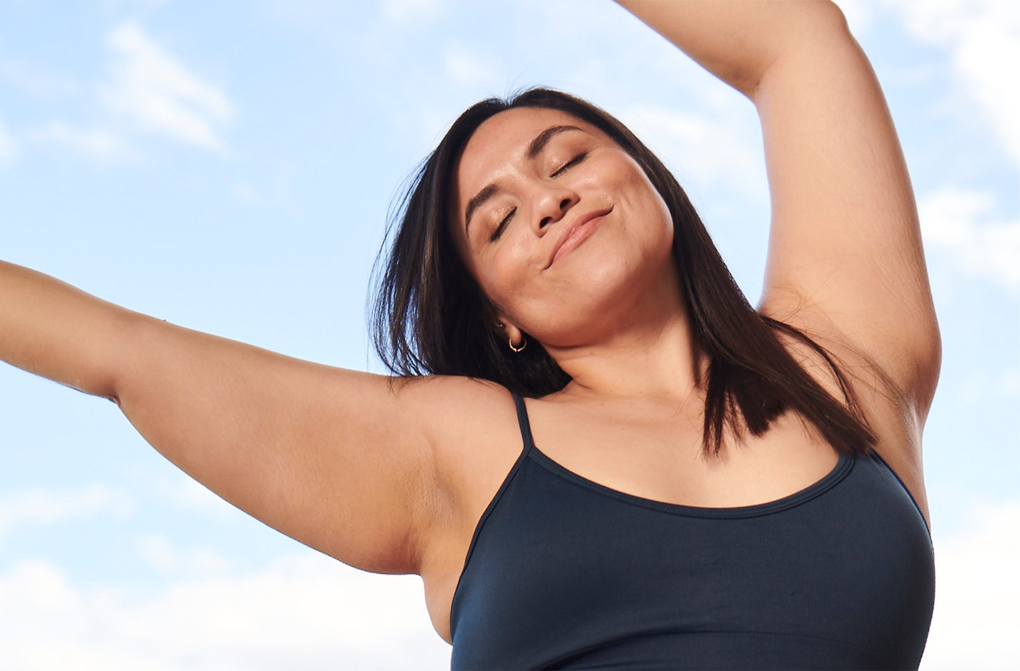 Smiling woman with arms in the air against blue sky backdrop