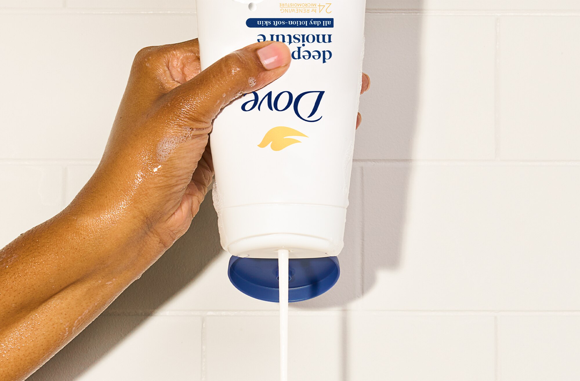 Hand squeezing a Dove body wash with product coming out of it