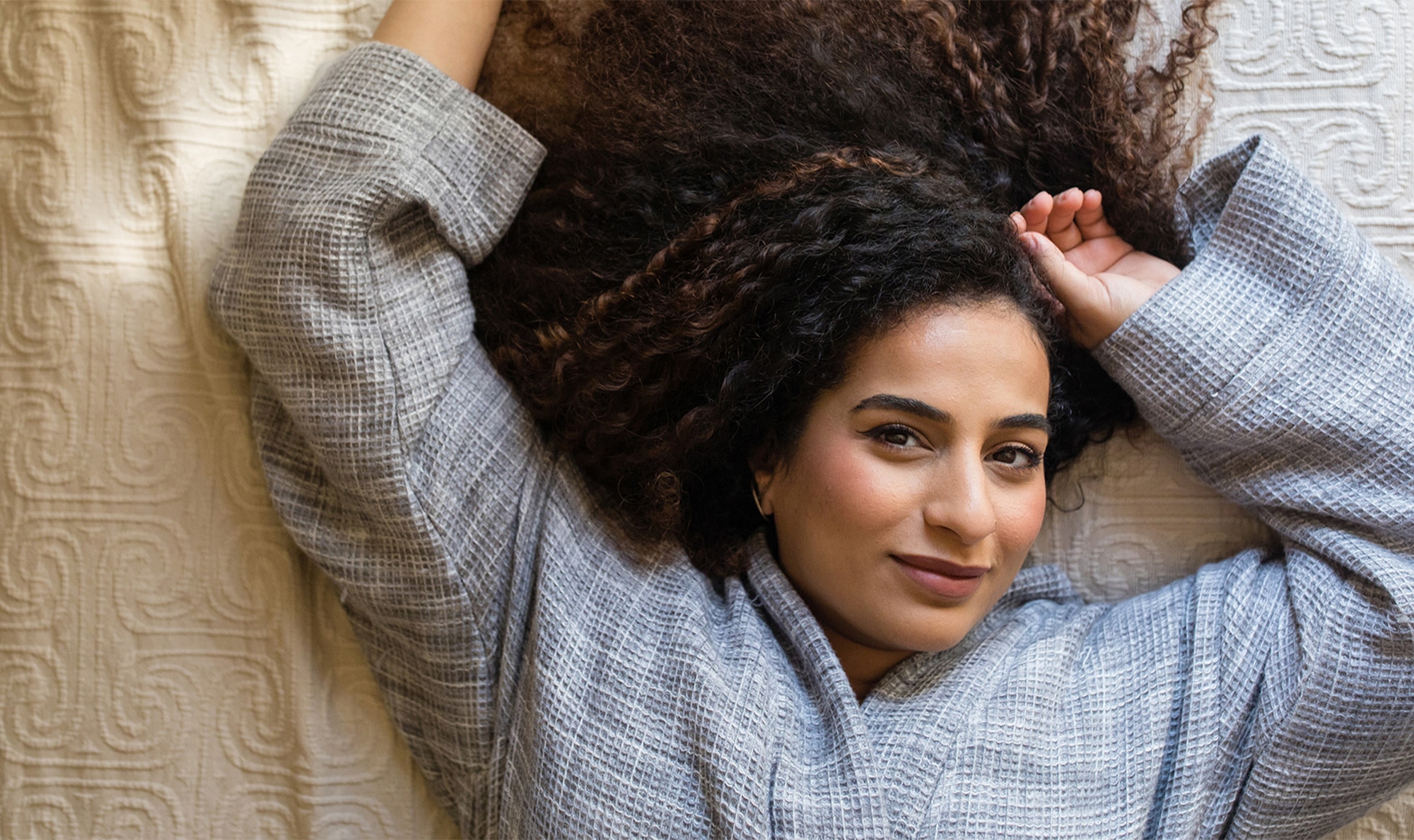 Woman with curly textured hair lying on a bed and looking up to the camera