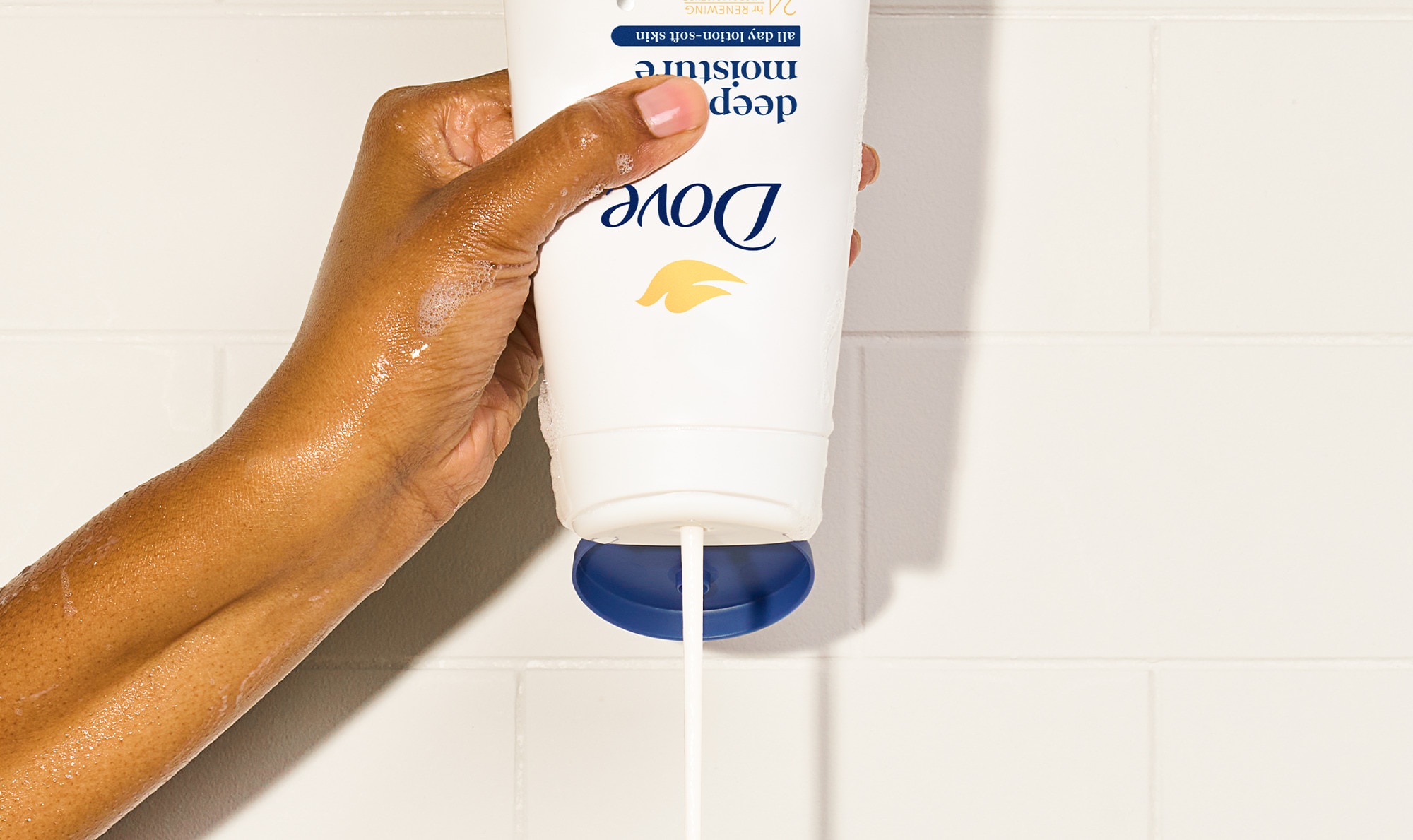 Hand squeezing a Dove body wash with product coming out of it