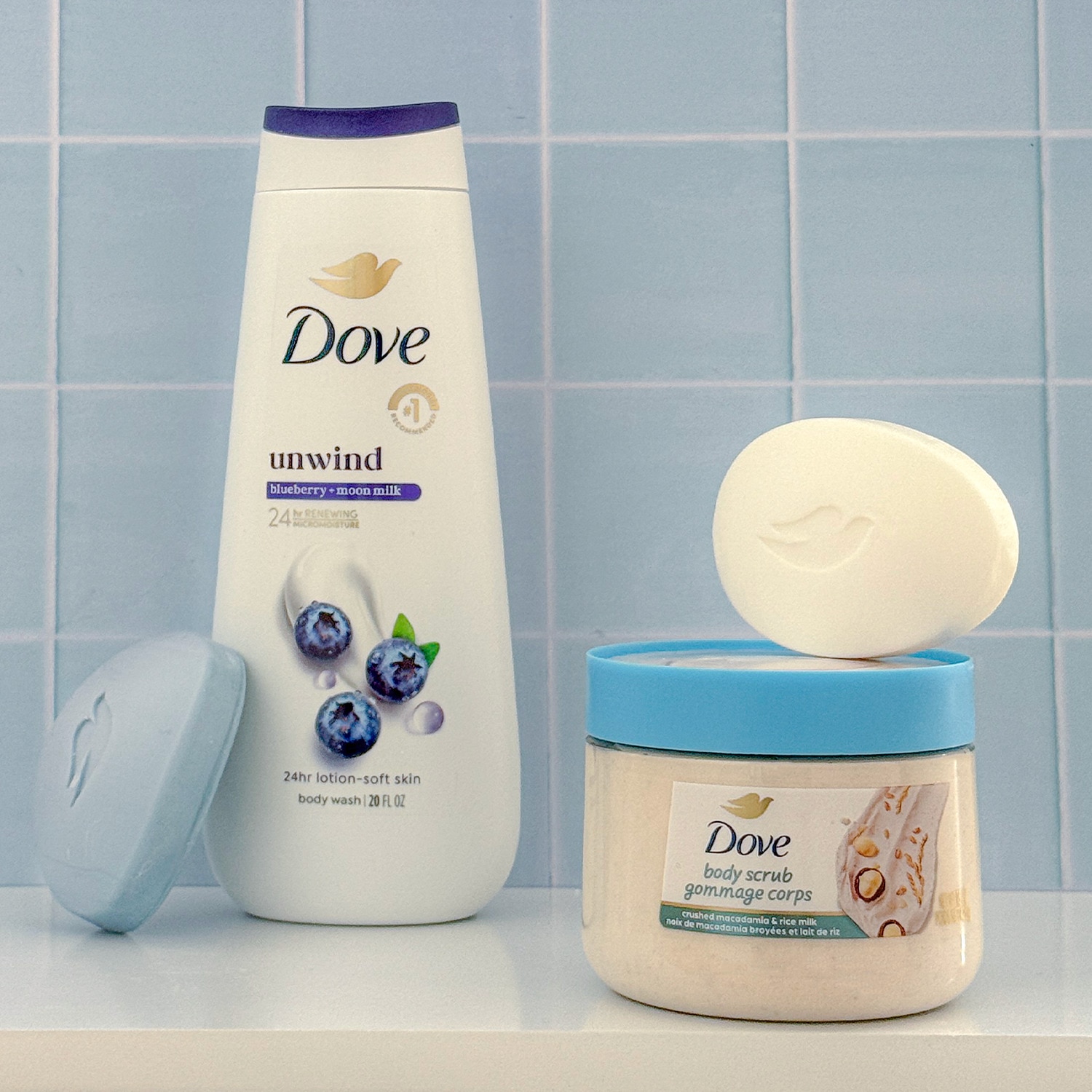 Product line up of Dove body wash, Beauty Bar and Body Scrub against blue bathroom tile background
