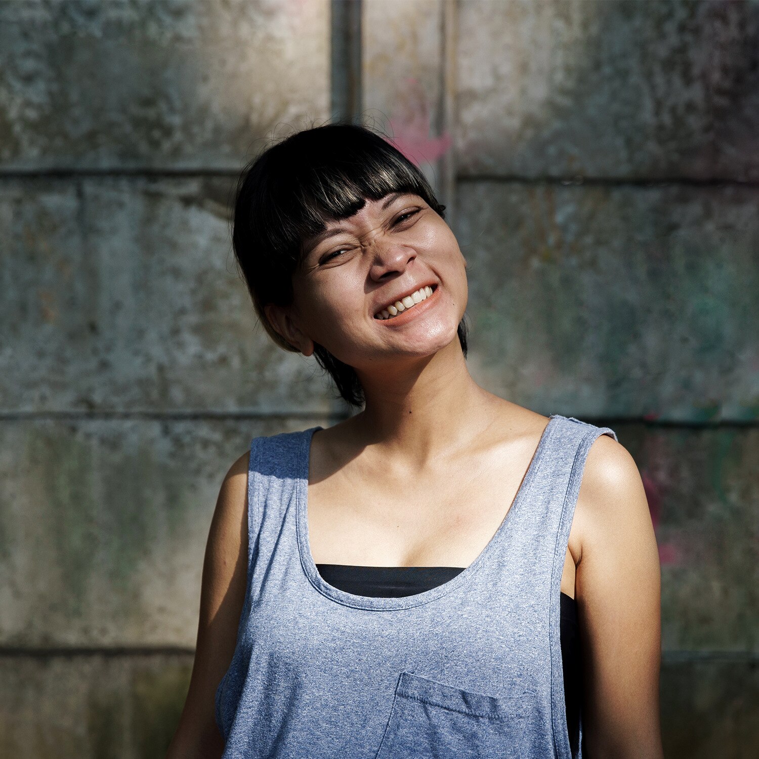 Image of woman in blue vest smiling and looking down the camera, with gentle sunlight on her face