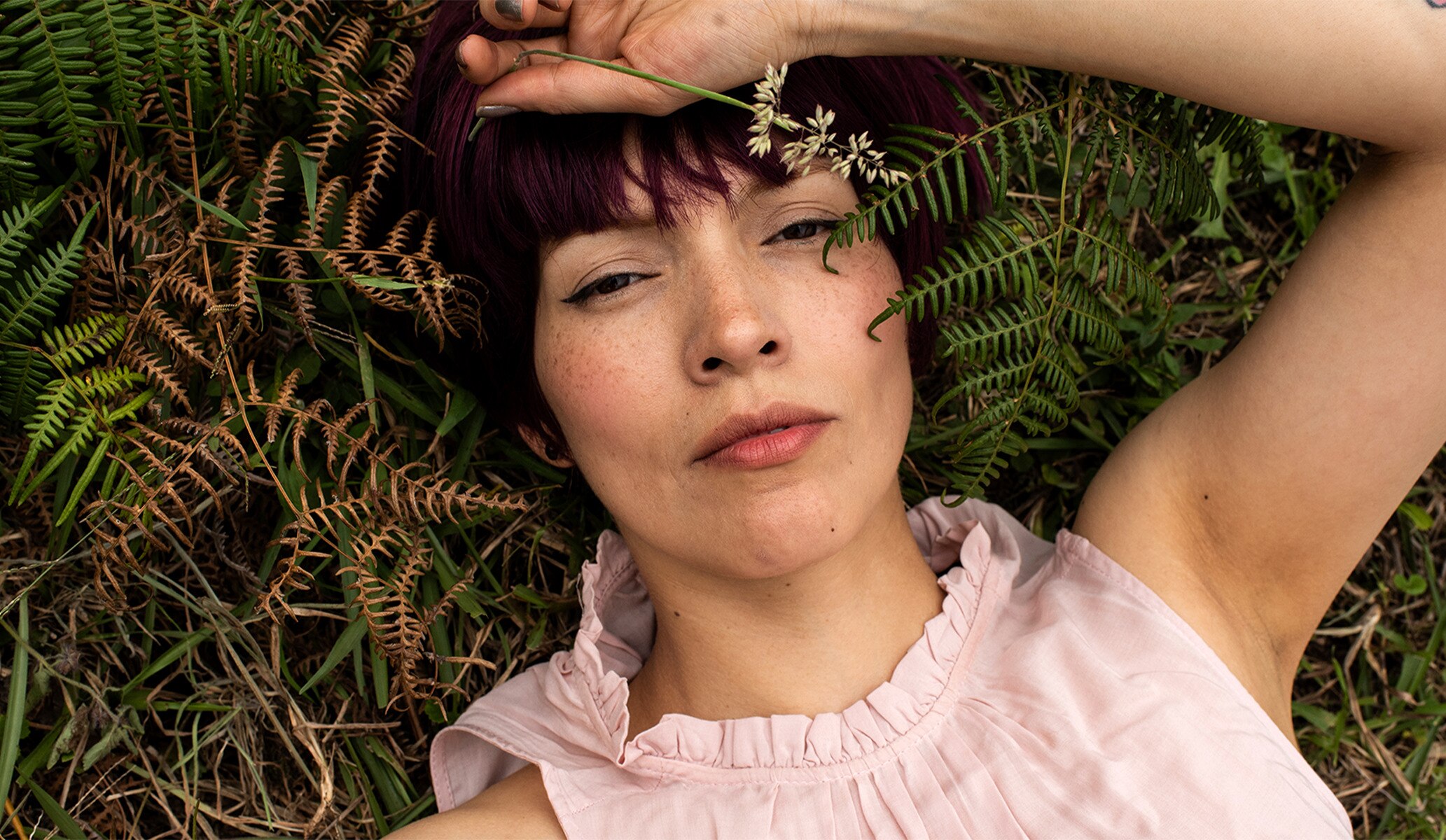 Image of woman in pink top lying on grass and looking down camera