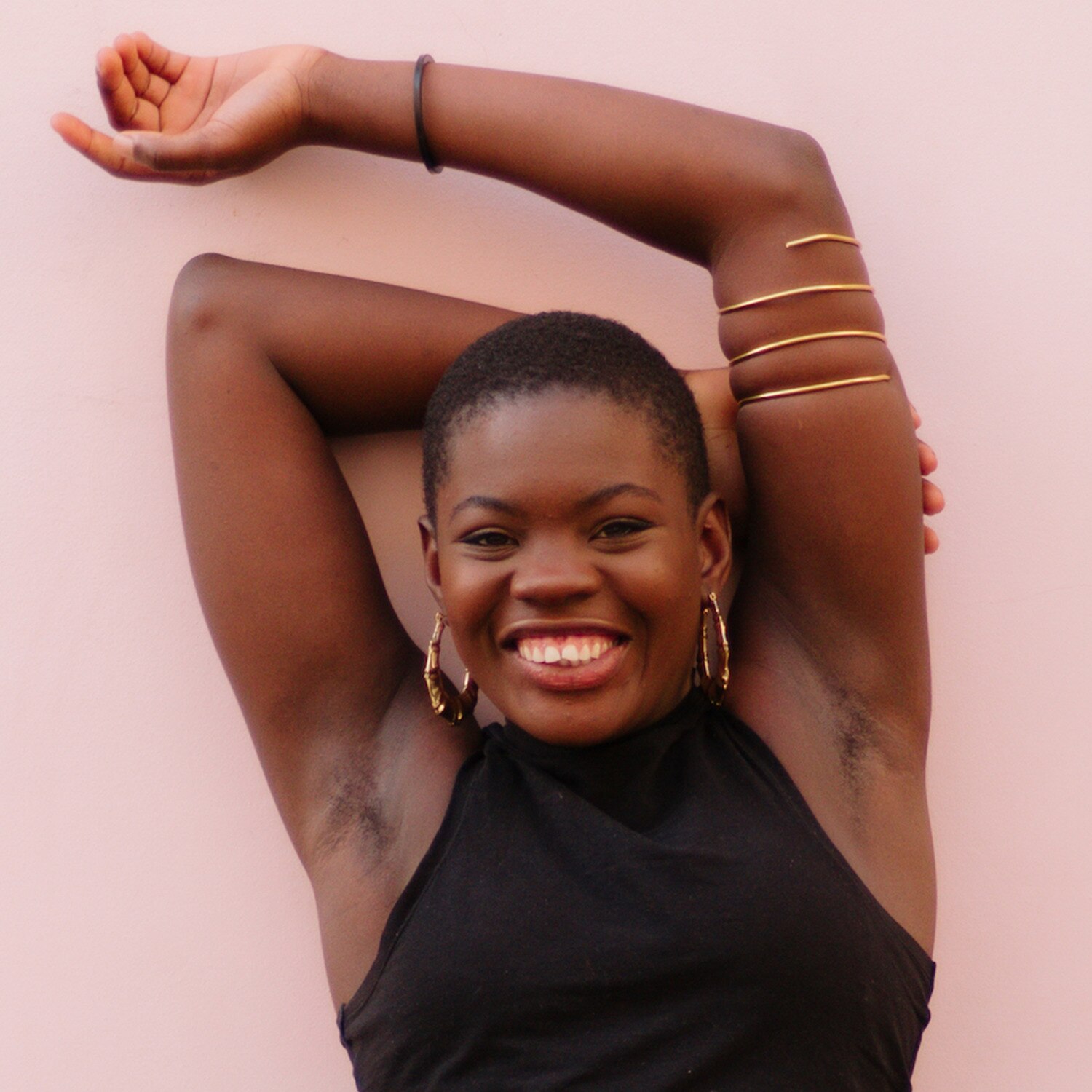 Image of smiling woman with arms over her head, standing against a pink wall