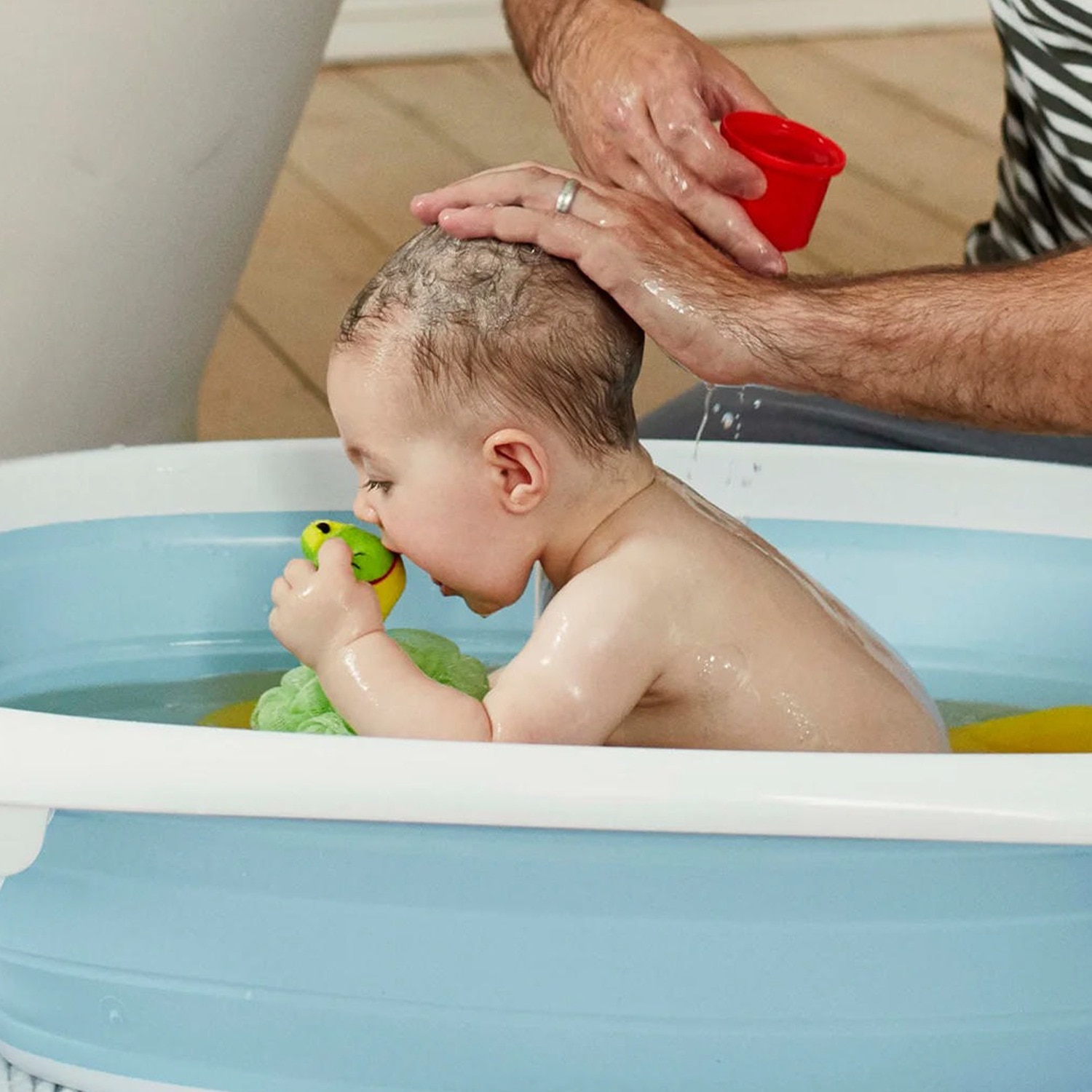 Image of a baby in a bath playing with a green dinosaur bath toy