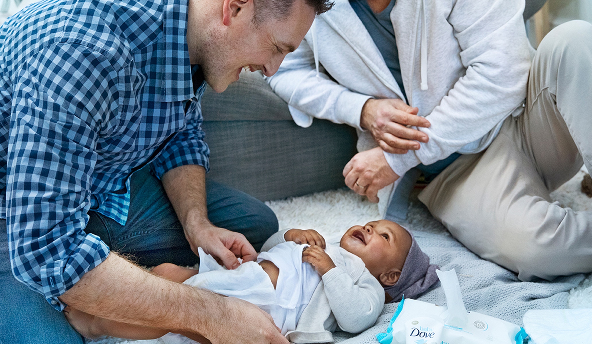 Image of a father smiling down at his baby on a blanket on the floor