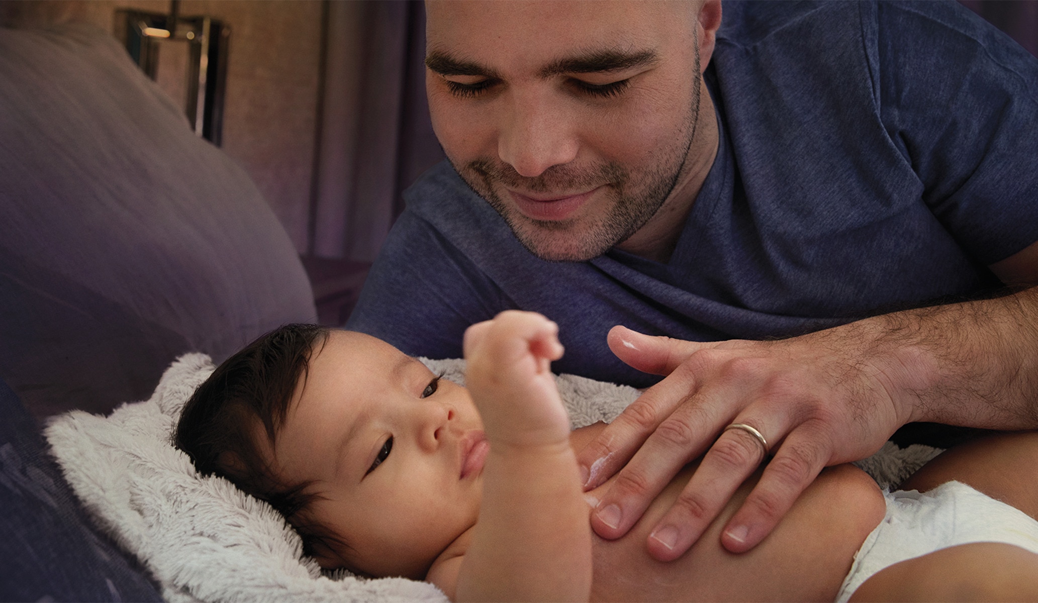 Image of a father smiling at his baby and resting a hand on their tummy
