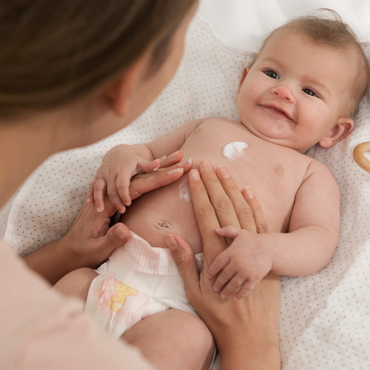 Baby lying on a blanket with their mother rubbing lotion into their tummy