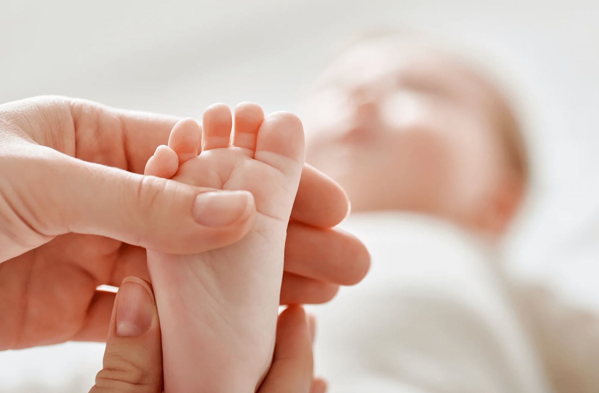 Mother holding her baby's foot, which is in focus. The rest of the baby is out of focus in the background