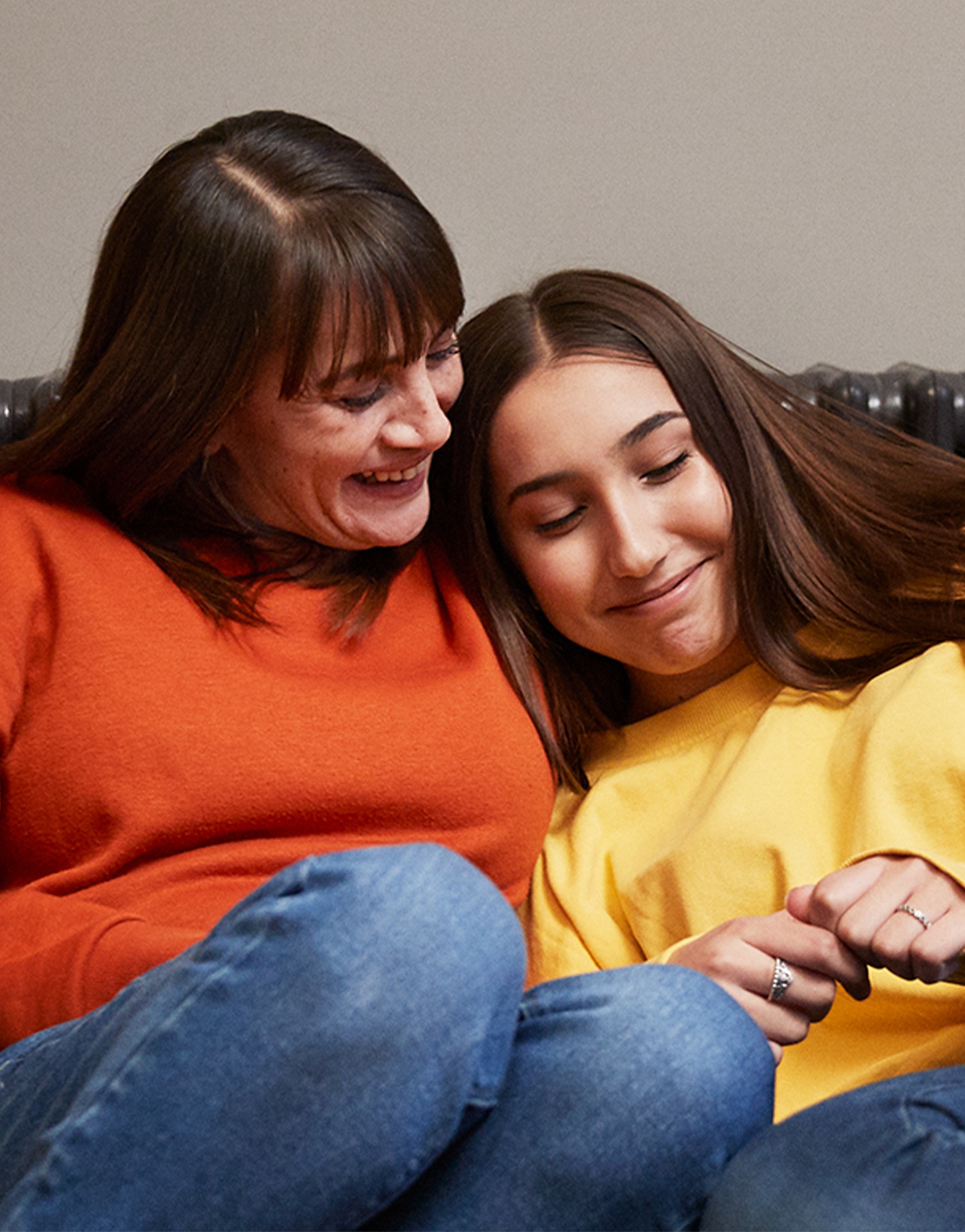 Mother and her daughter smiling and sitting together on a sofa