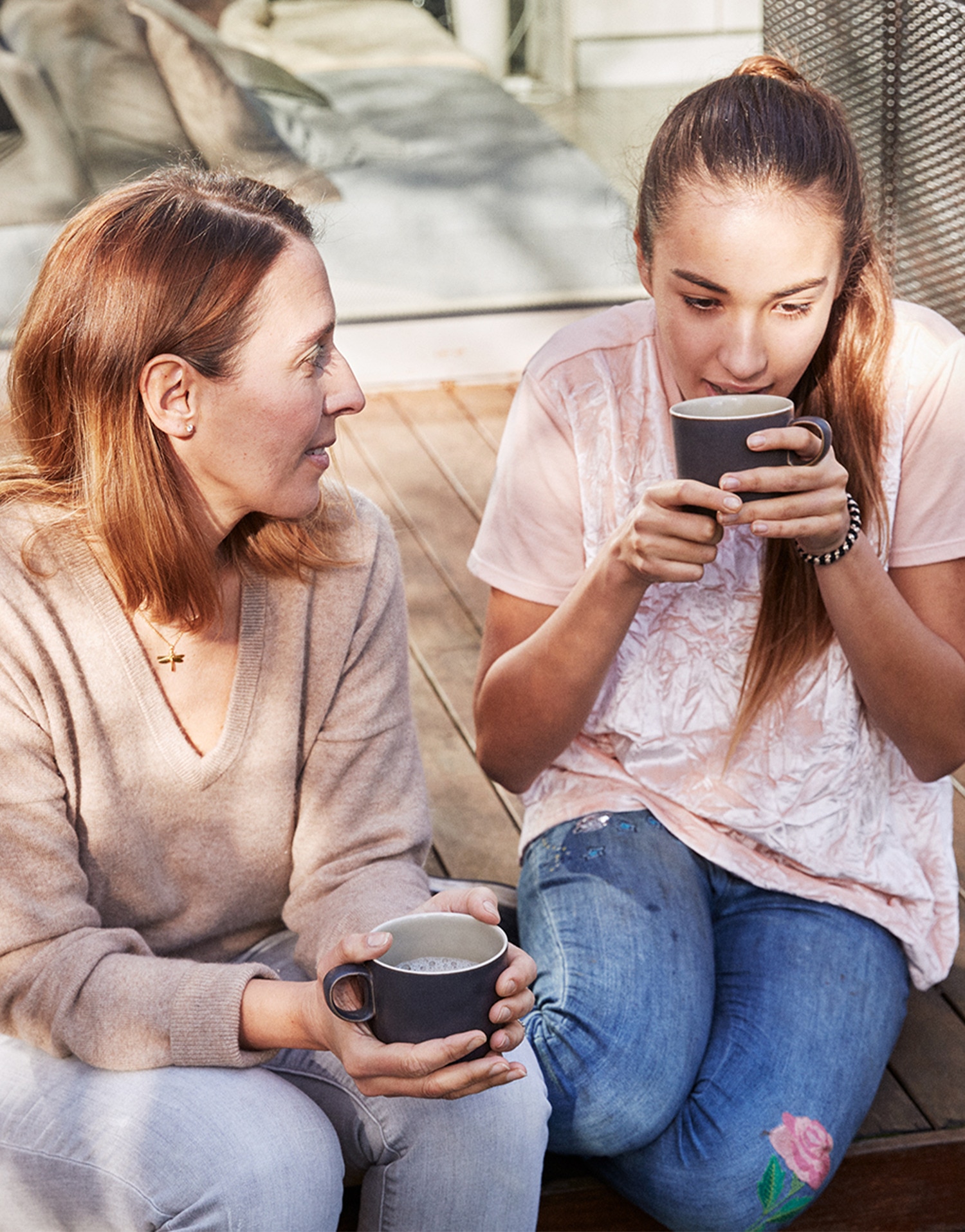 Mother and her teenage daughter enjoying a hot drink together on a sofa