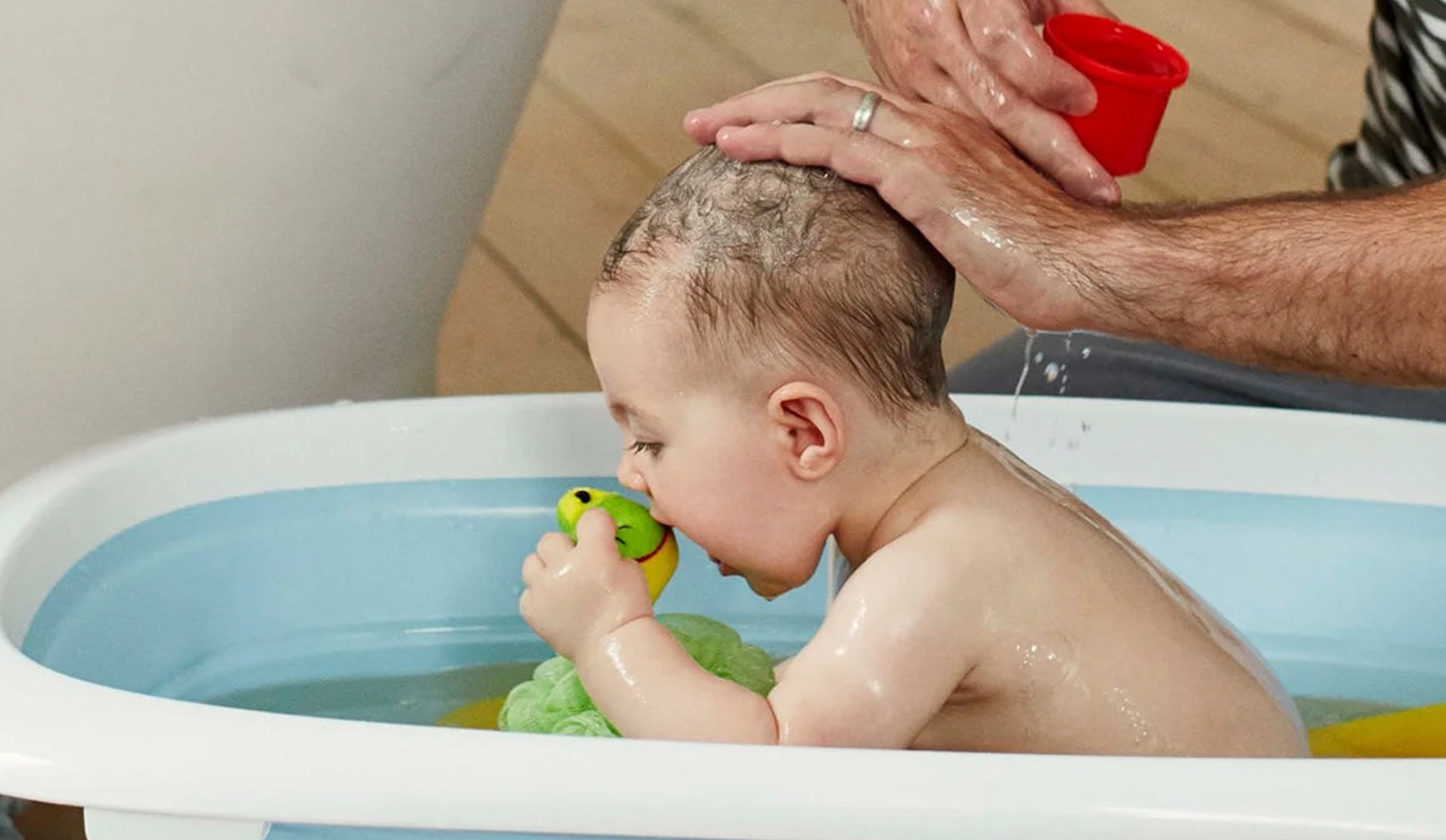 Image of a baby in a bath playing with a green dinosaur bath toy