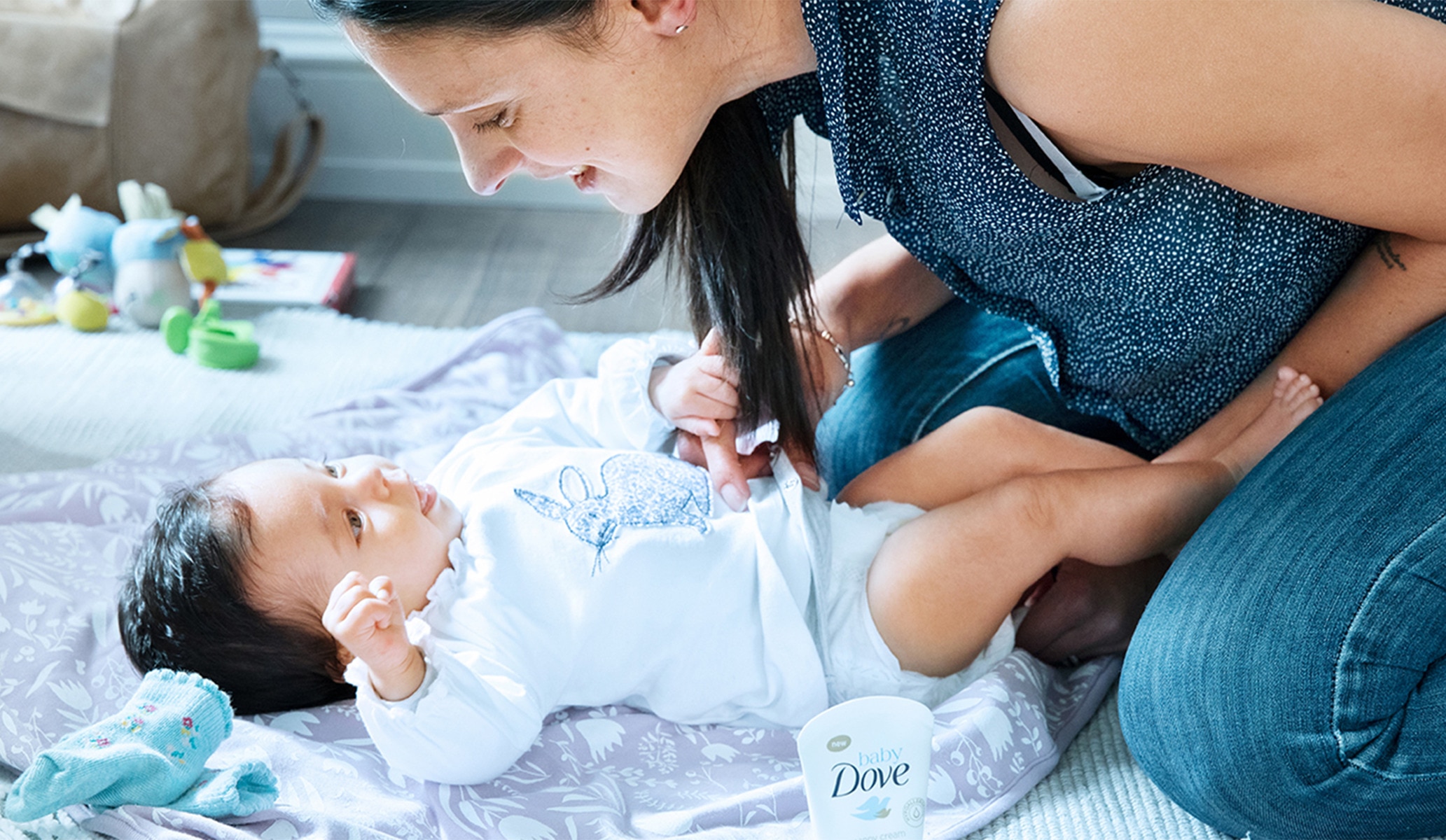 Image of a baby smiling up at their mother from a blanket on the floor