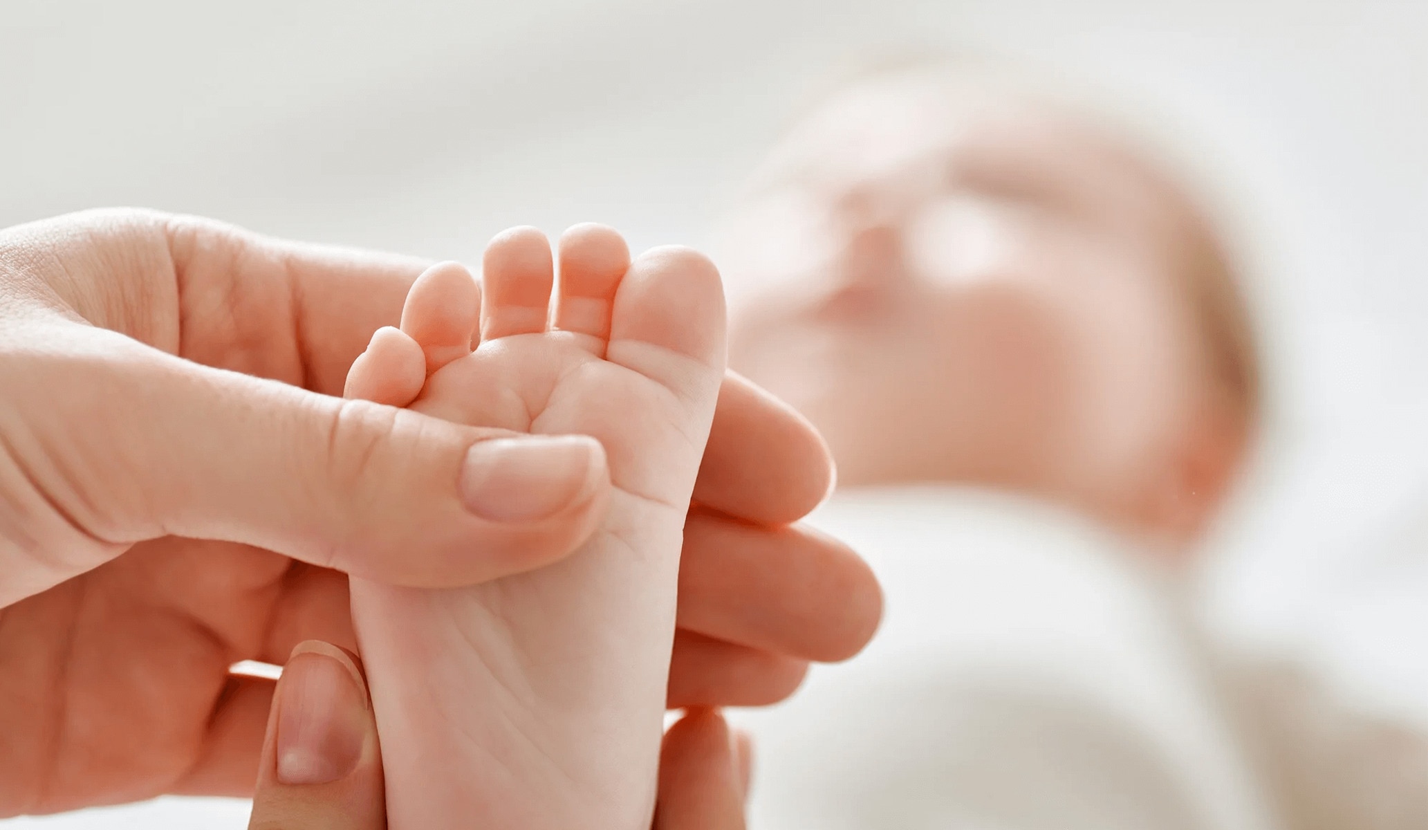 Image of a mother holding her baby's foot, which is in focus. The rest of the baby is out of focus in the background