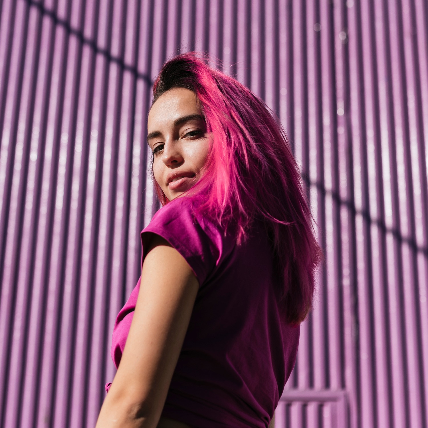 Woman with pink hear looks over her shoulder at the camera