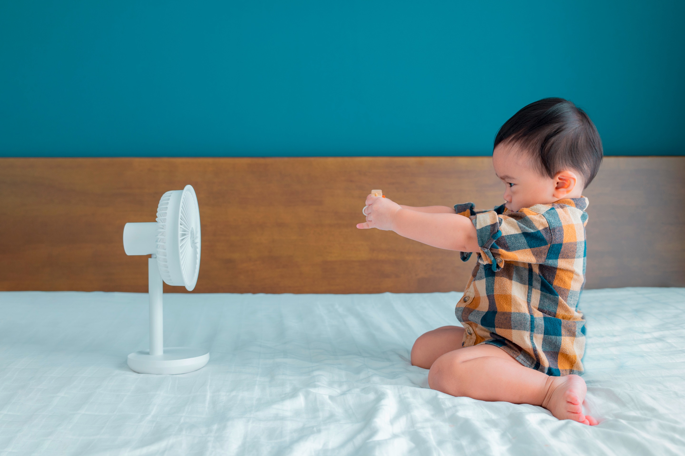 A baby plays in front of an electric fan