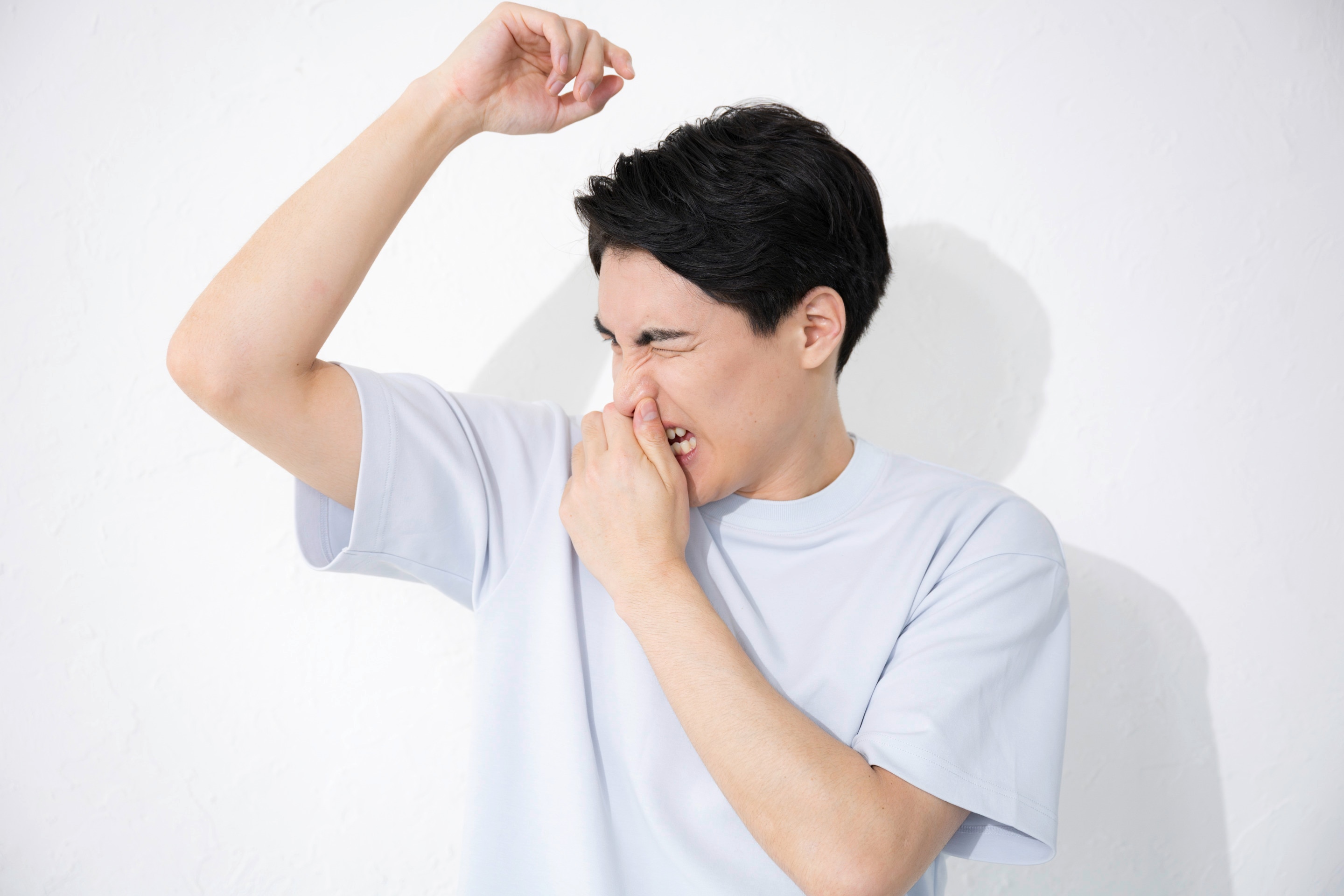 Pria Asia sedang mengangkat tangan dan menutup hidung karena bau ketiak yang menyengat