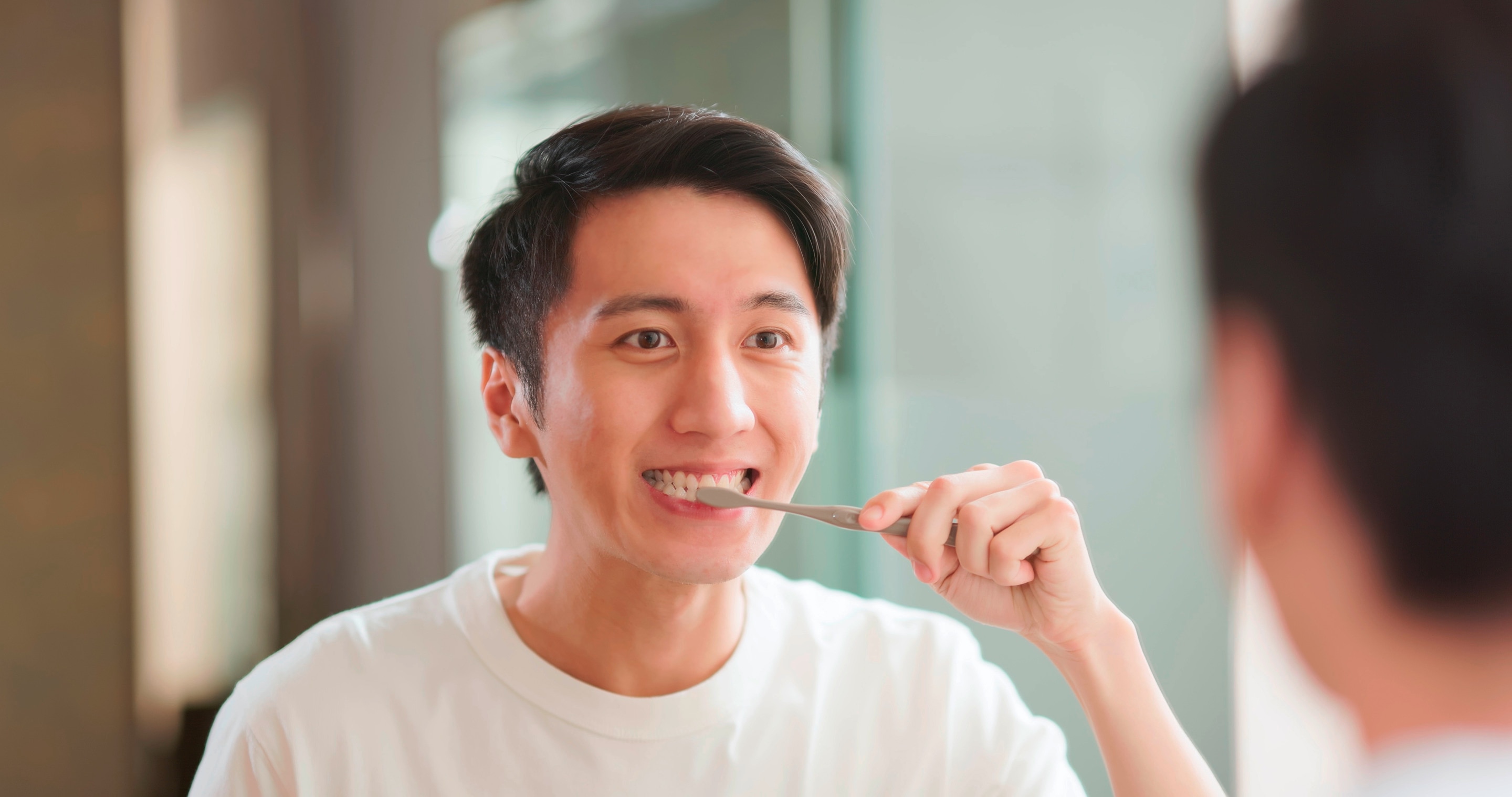 An Asian man brushing his teeth.