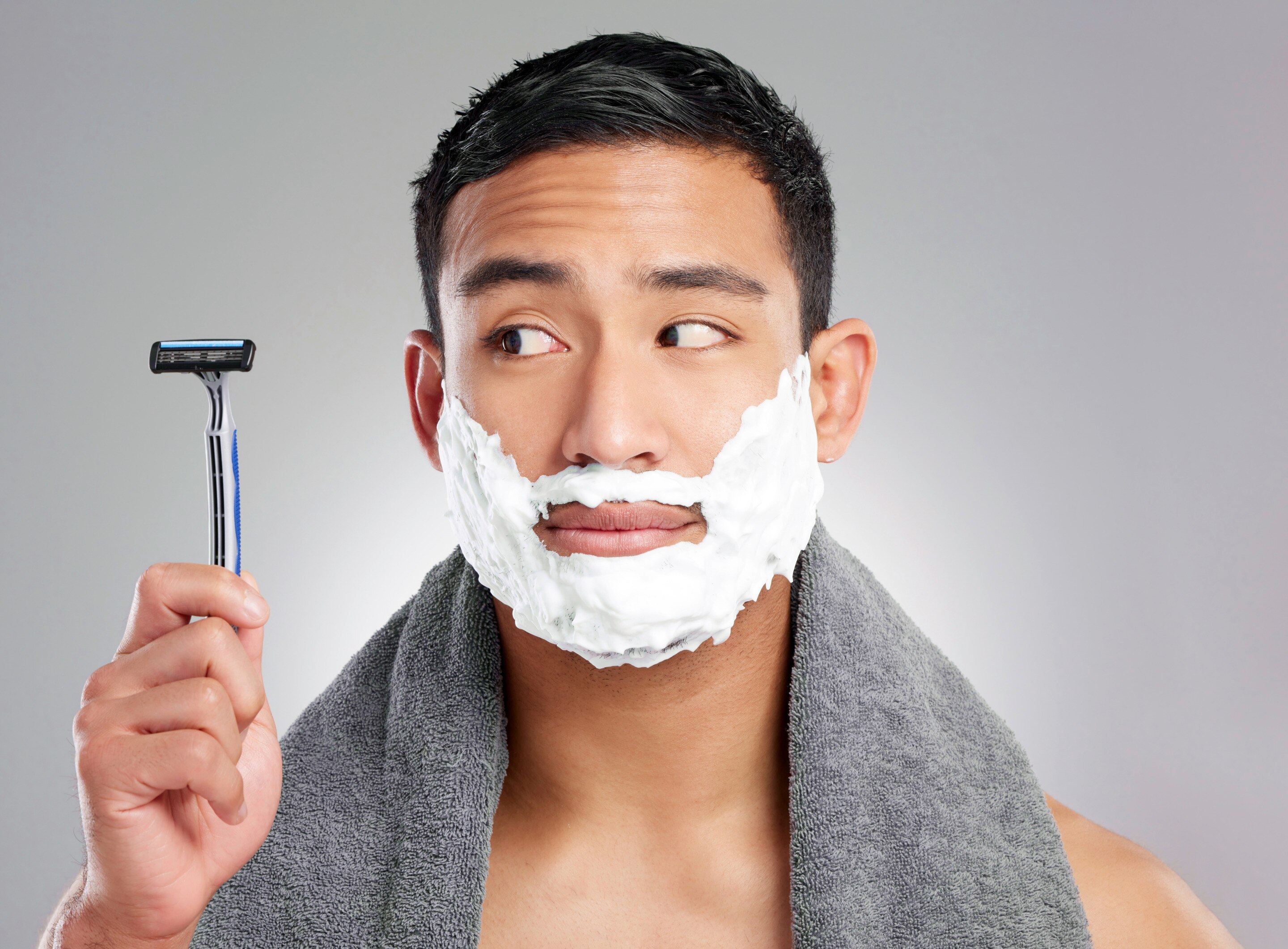 An Asian man with shaving cream on his face and holding a shaver.