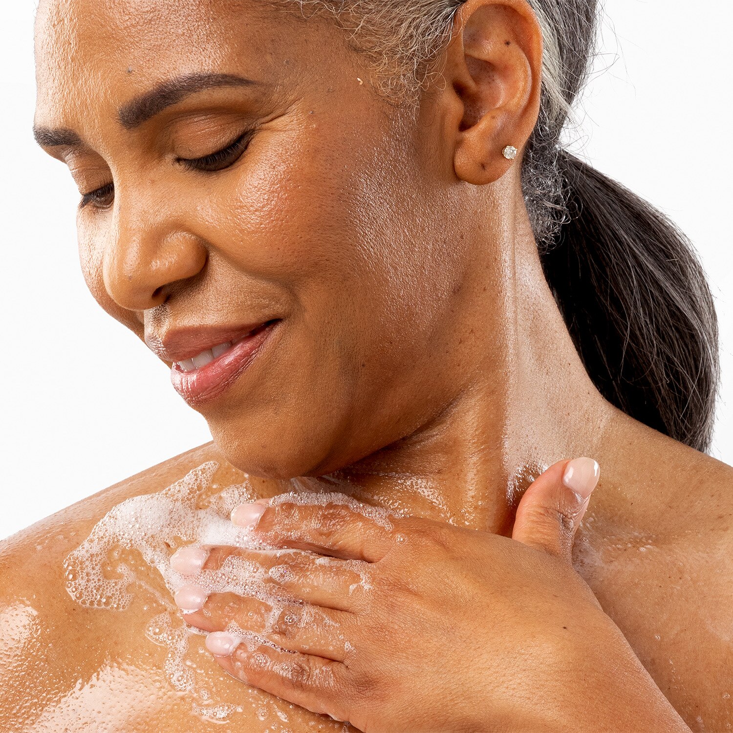 A woman lathering body wash on her upper shoulder