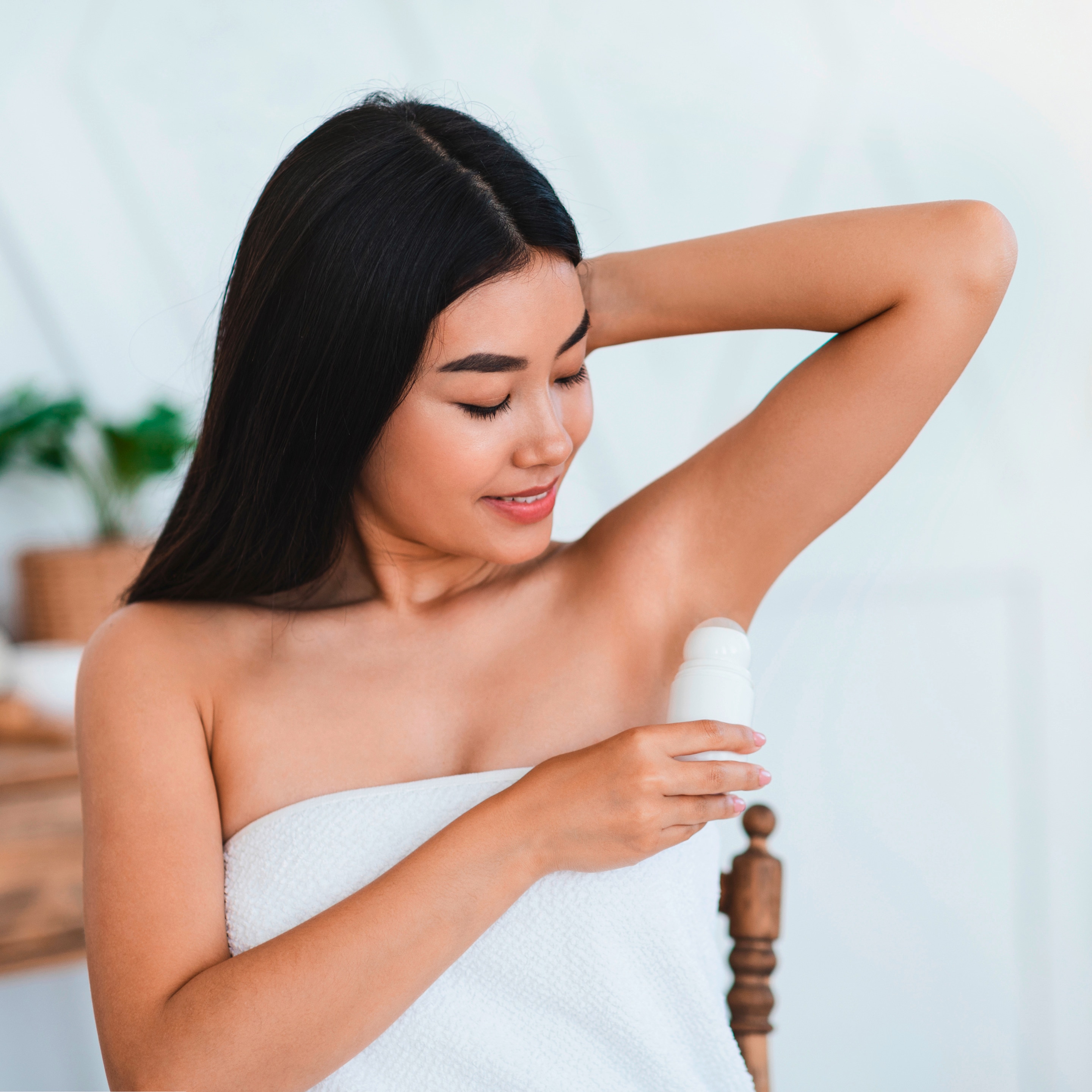 A woman holds up a roll-on deodorant up to her armpits.