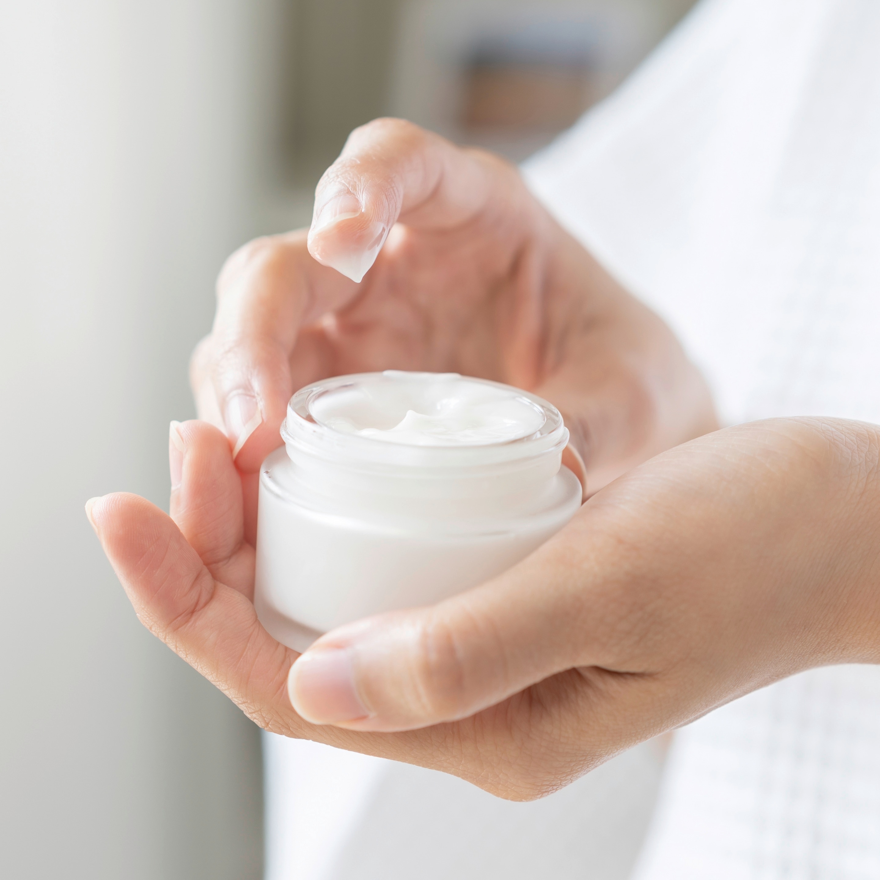 Woman’s hand holding a tub of moisturizer.