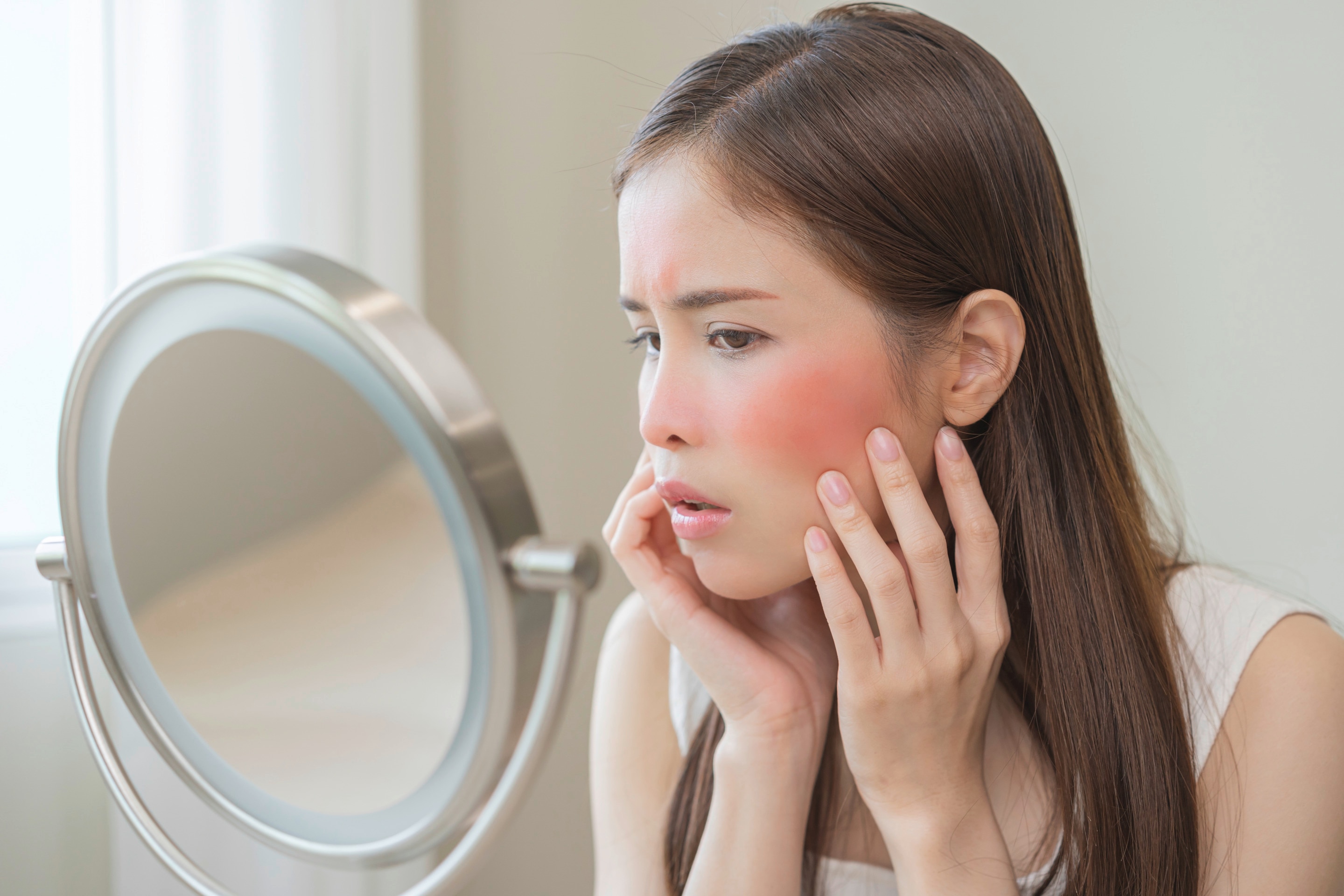 Asian woman with skin redness looking at mirror.