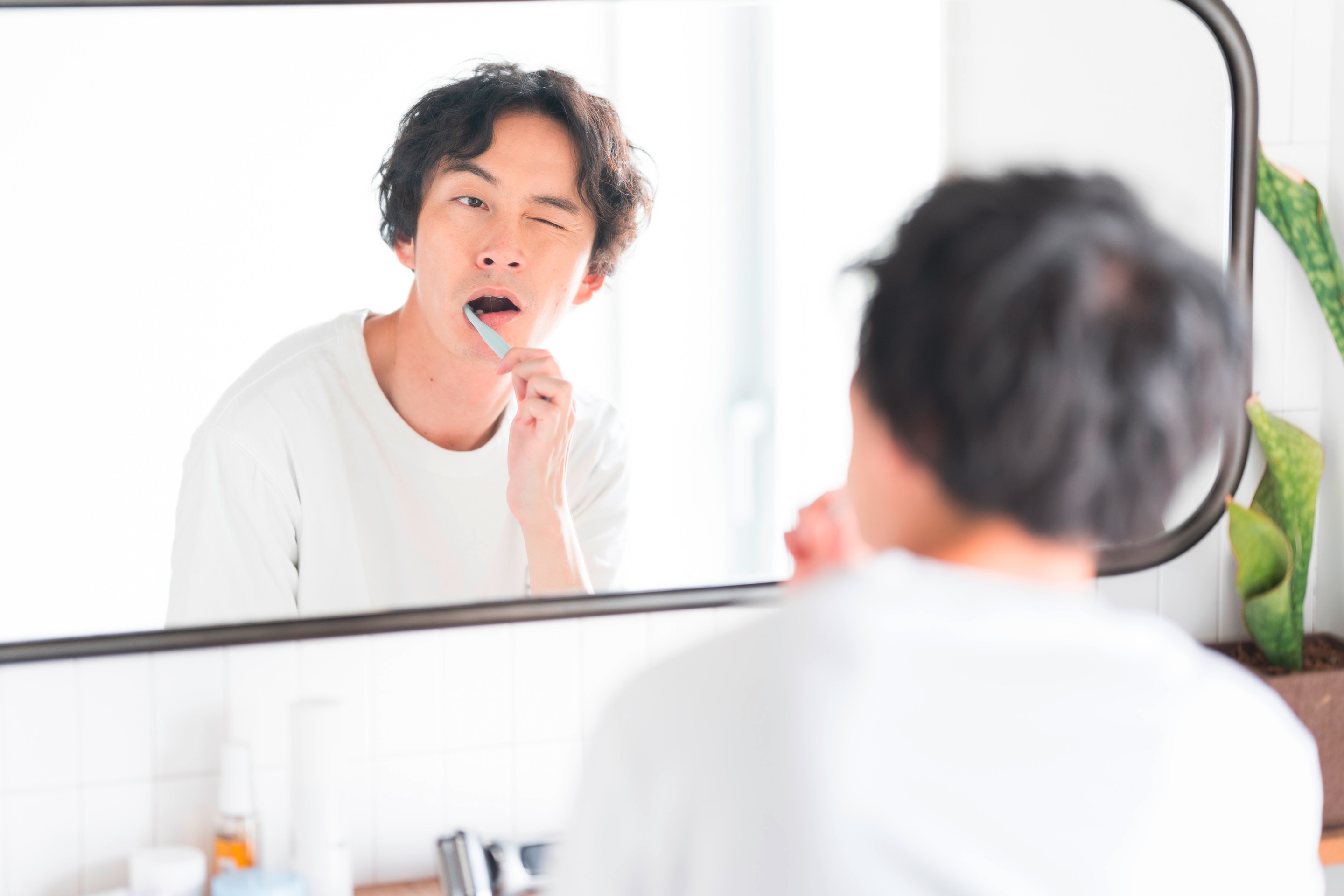Man brushes his teeth in front of a mirror.