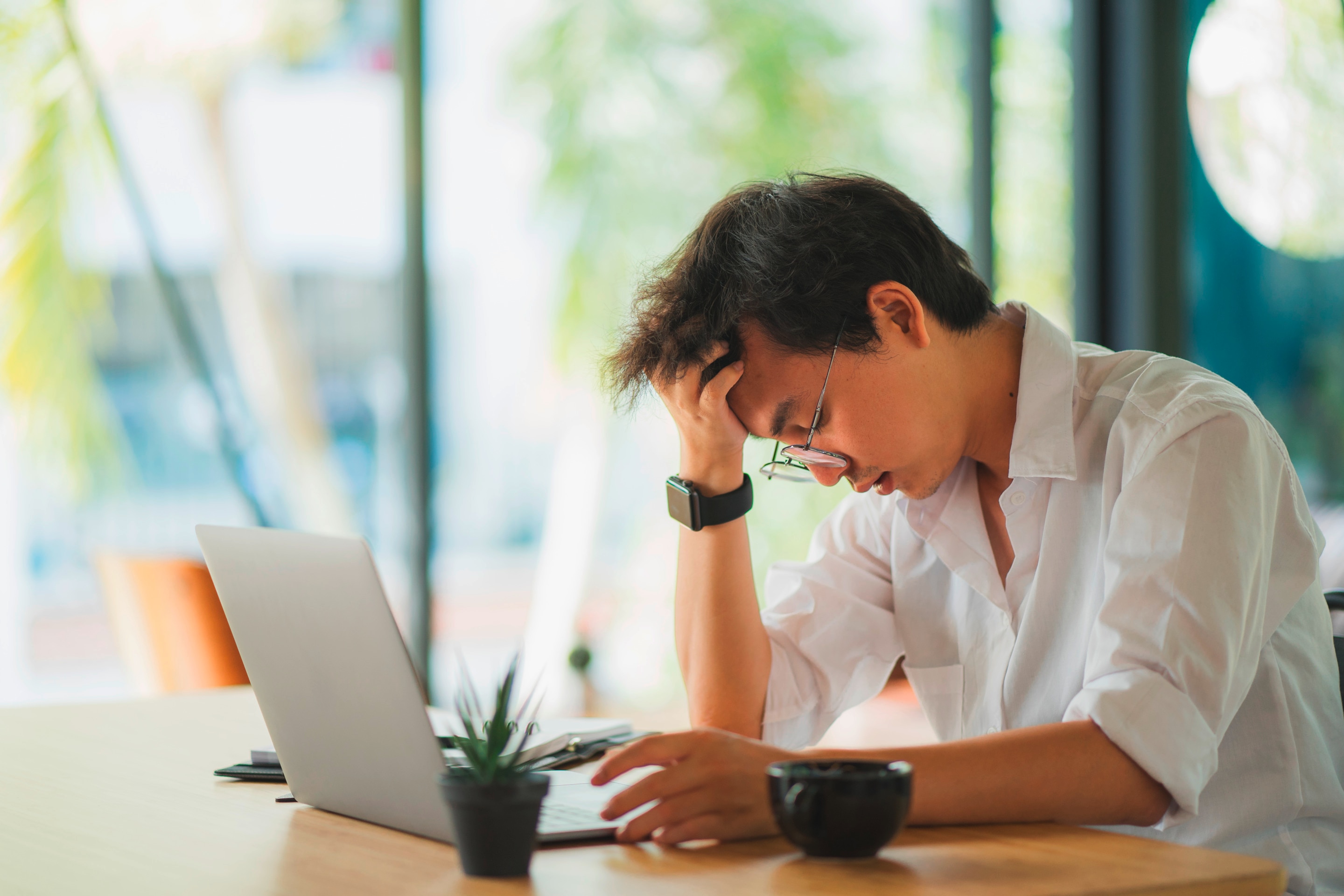 A stressed man holds a part of his hair while in front of a laptop.