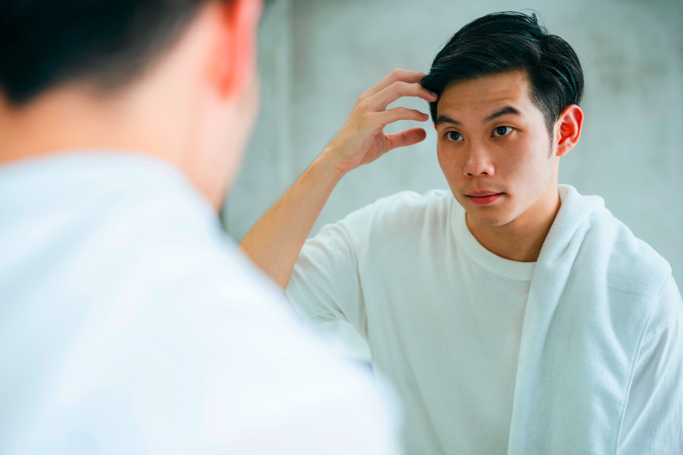 A young man checks his hair in the mirror.