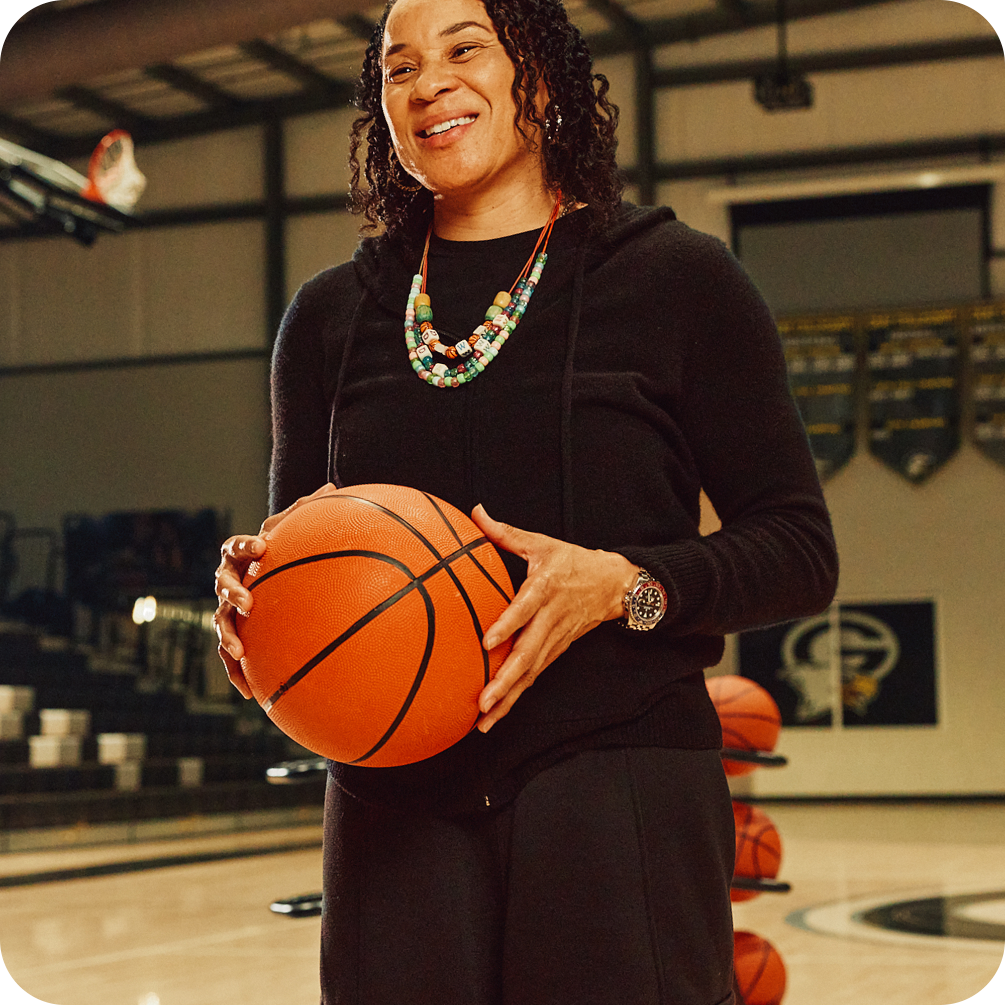Dawn Staley smiling whilst holding a basketball on a basketball court