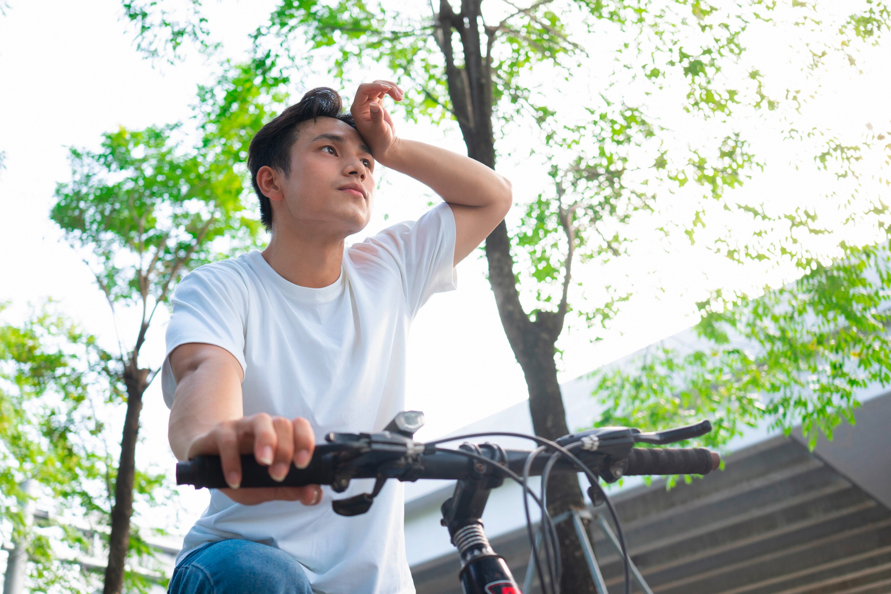 Man riding bike outdoors, wiping his sweat.
