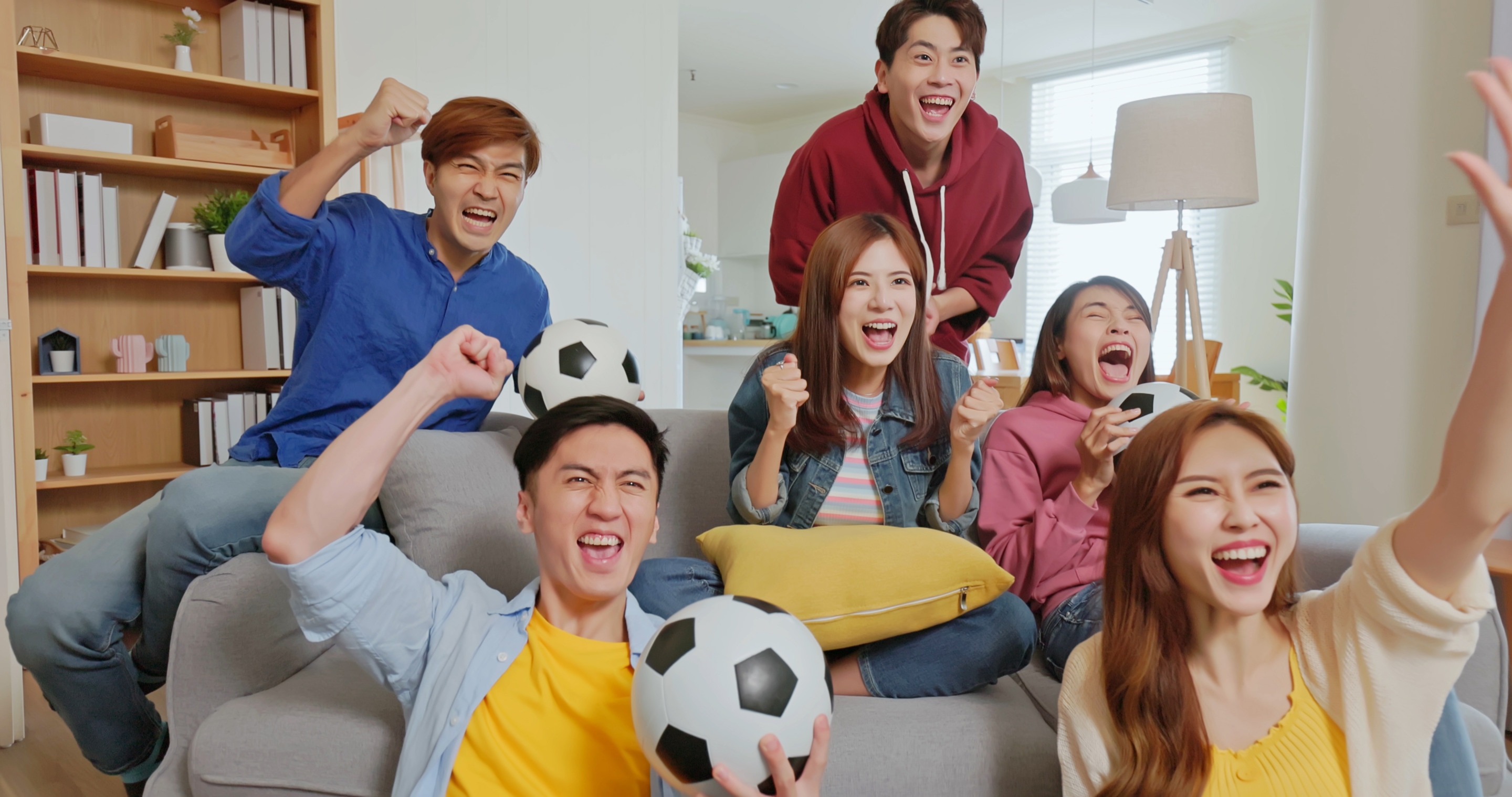 Grup Pria dan Wanita Asia sedang duduk di sofa sambil menonton bola bersama
