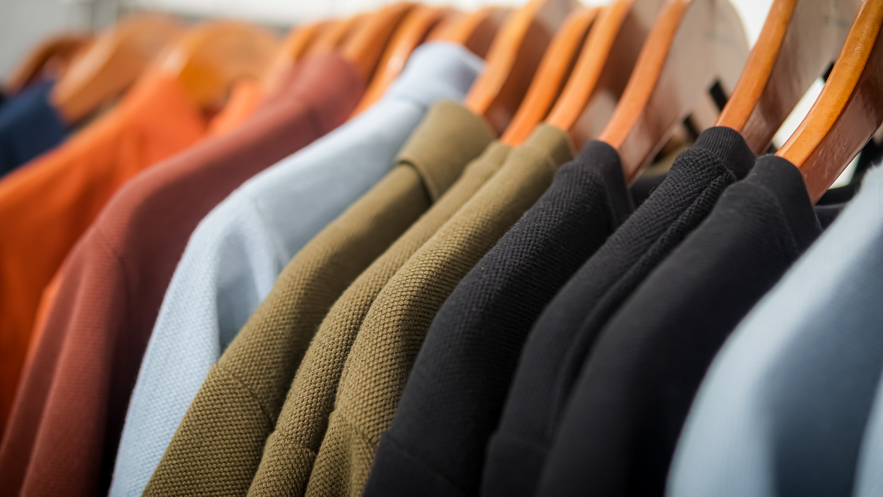 beberapa baju berwarna netral yang digantung rapi di hanger kayu, menampilkan tekstur kain yang berbeda-beda.