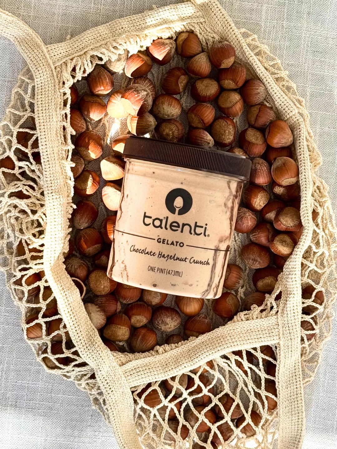 A pint of Talenti Chocolate Hazelnut Crunch Gelato placed in a bag of hazelnuts