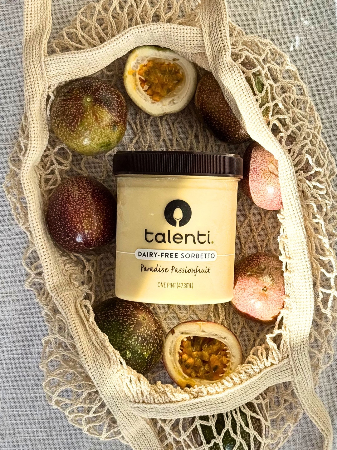 A pint of Talenti Paradise Passionfruit Sorbetto placed in a bag containing whole and cut passionfruit